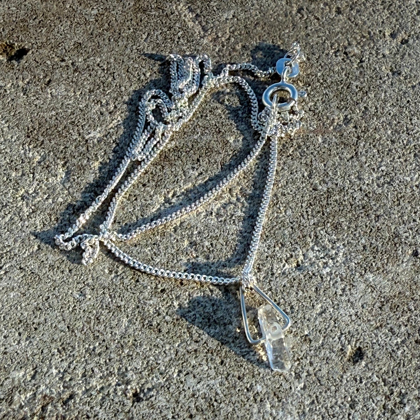 Silver necklace with petit eclear quartz on a textured gray surface