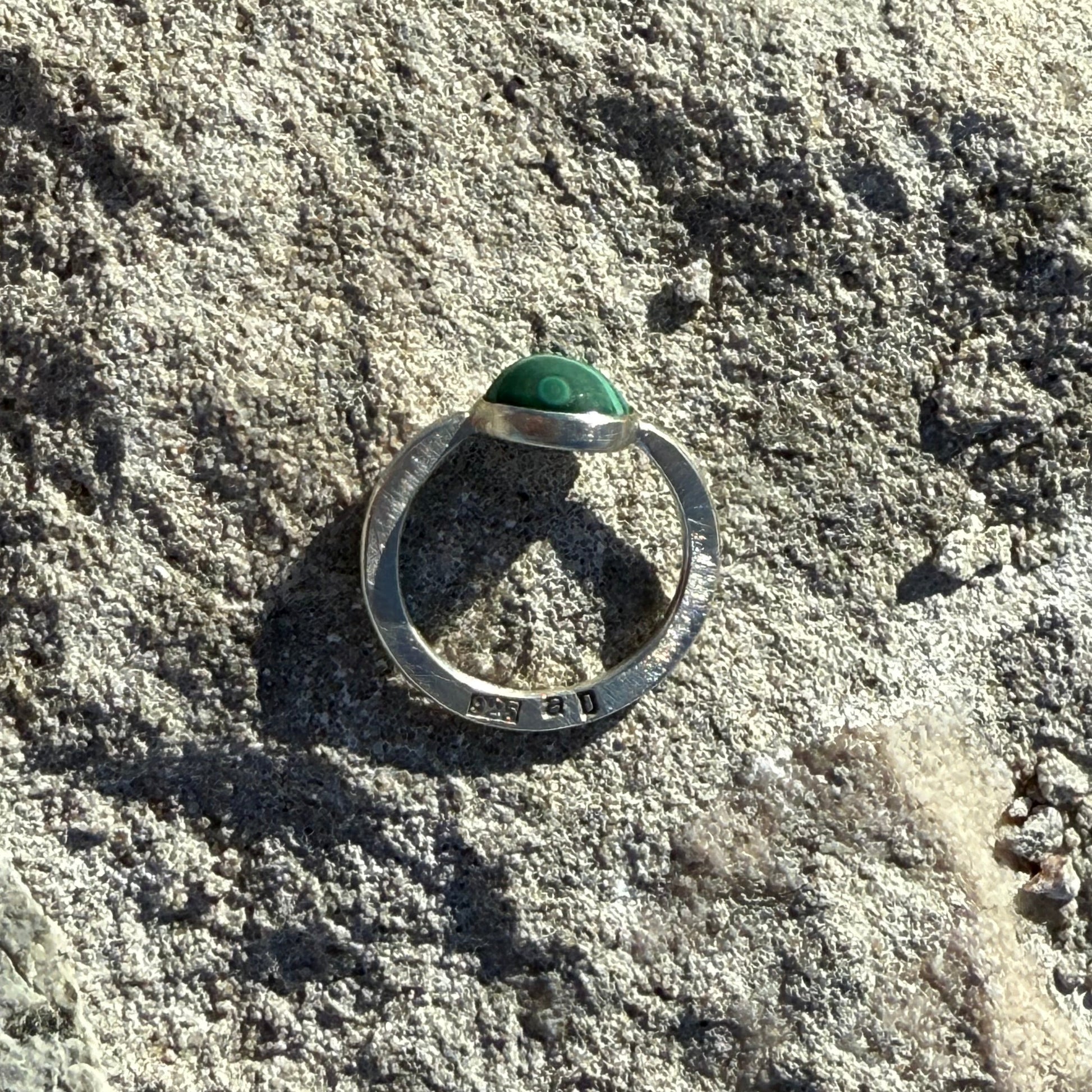Silver 925 ring with a green malachite stone on a textured rock surface