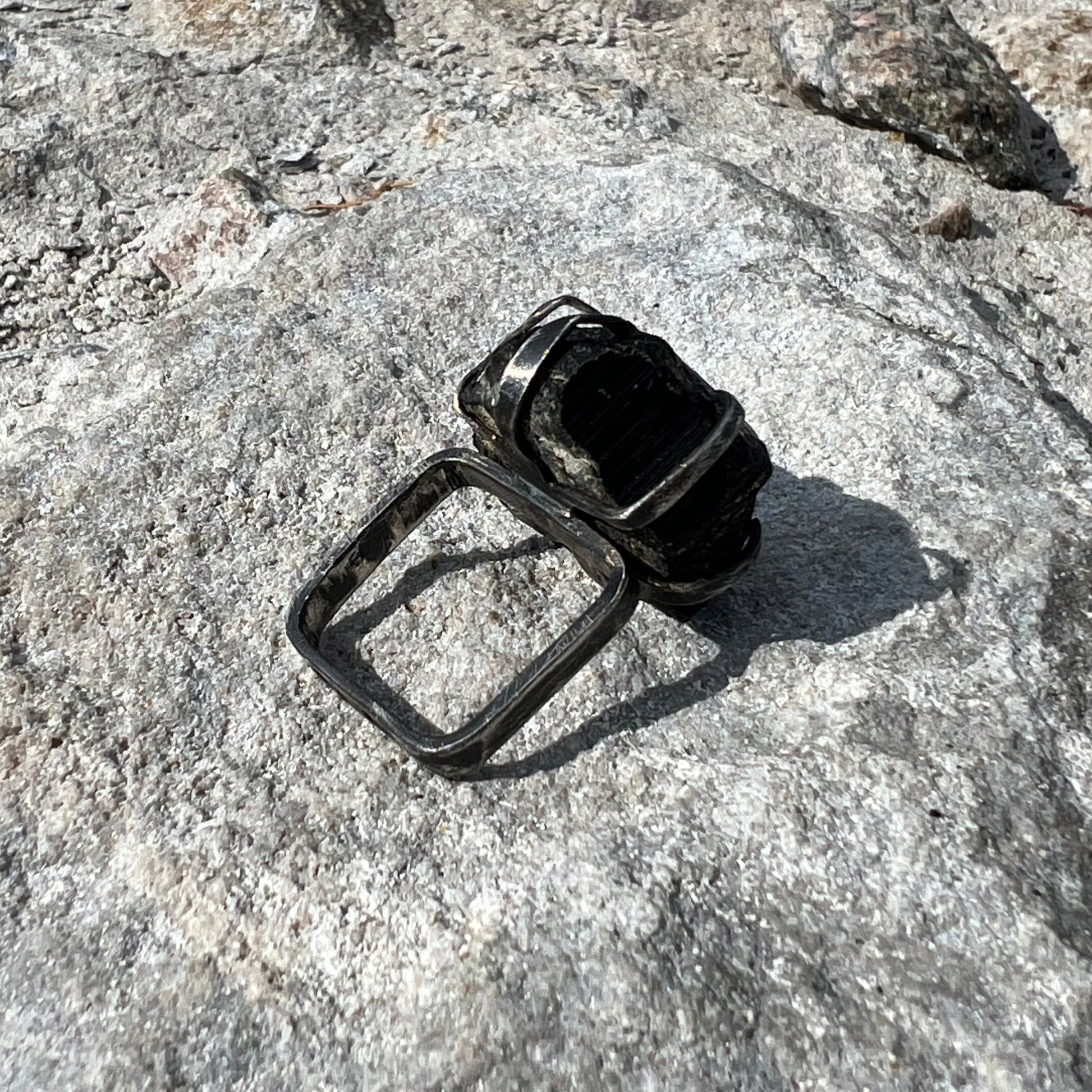 Raw Black Tourmaline crystal on a square ring band in oxidized silver on a textured stone surface