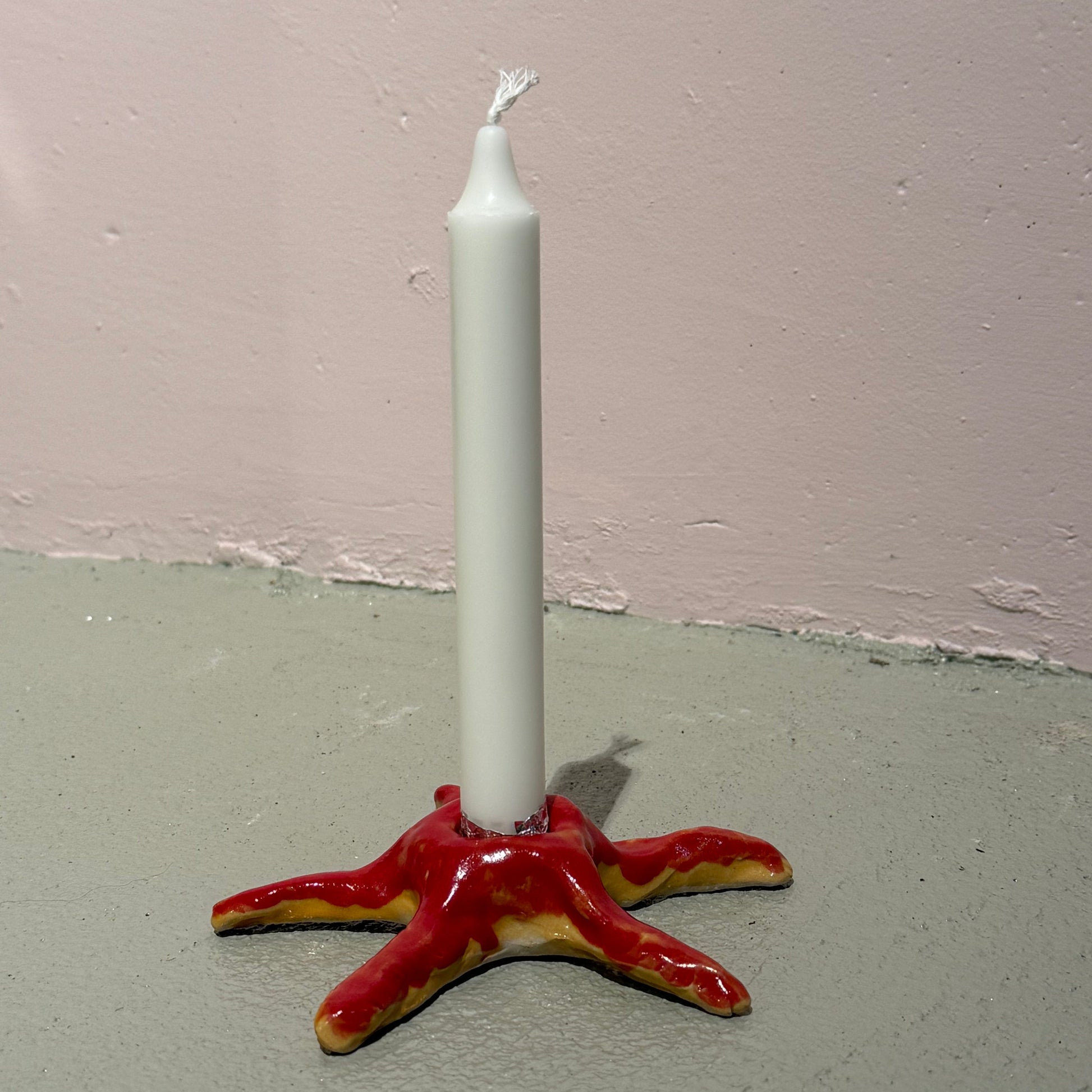 White candle in a red ceeramic starfish candle holder against a plain wall.