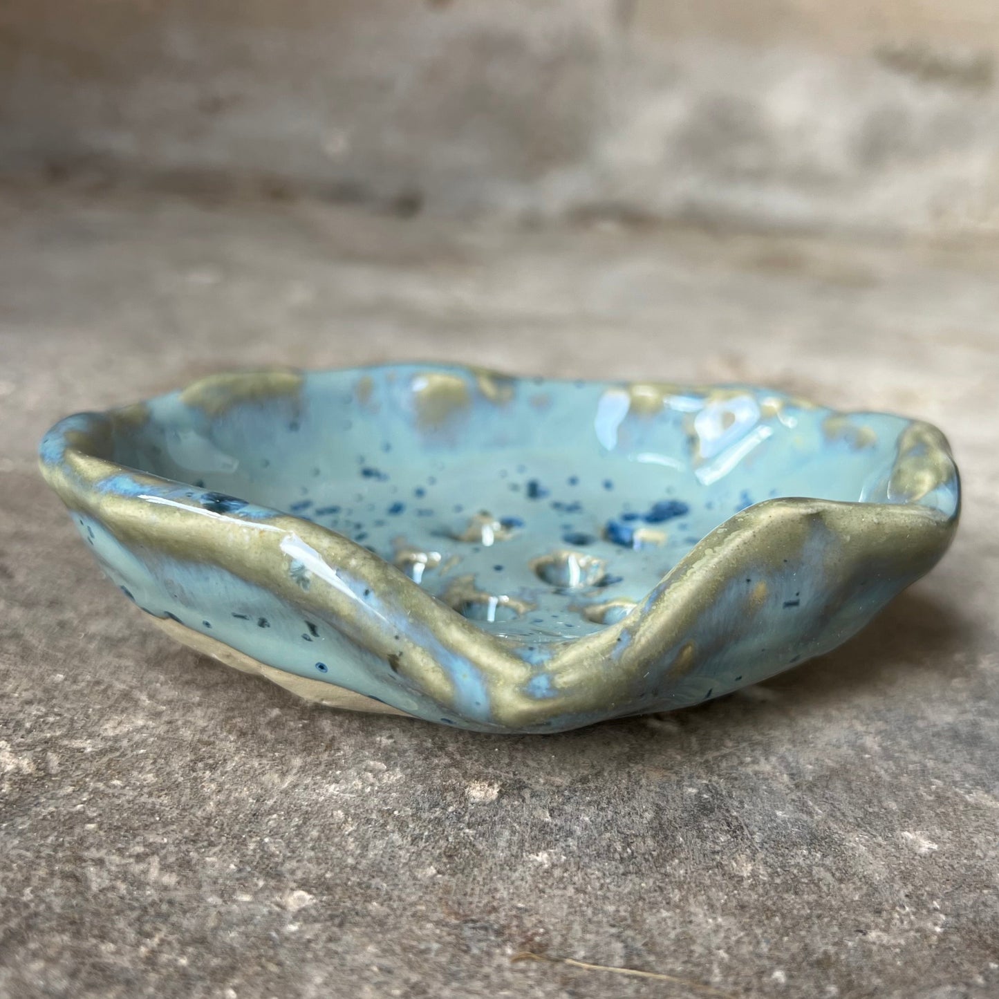 Ceramic soap dish with blue and green glaze on a concrete surface