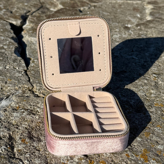 Open soft pink jewelry case with mirror on a textured stone surface