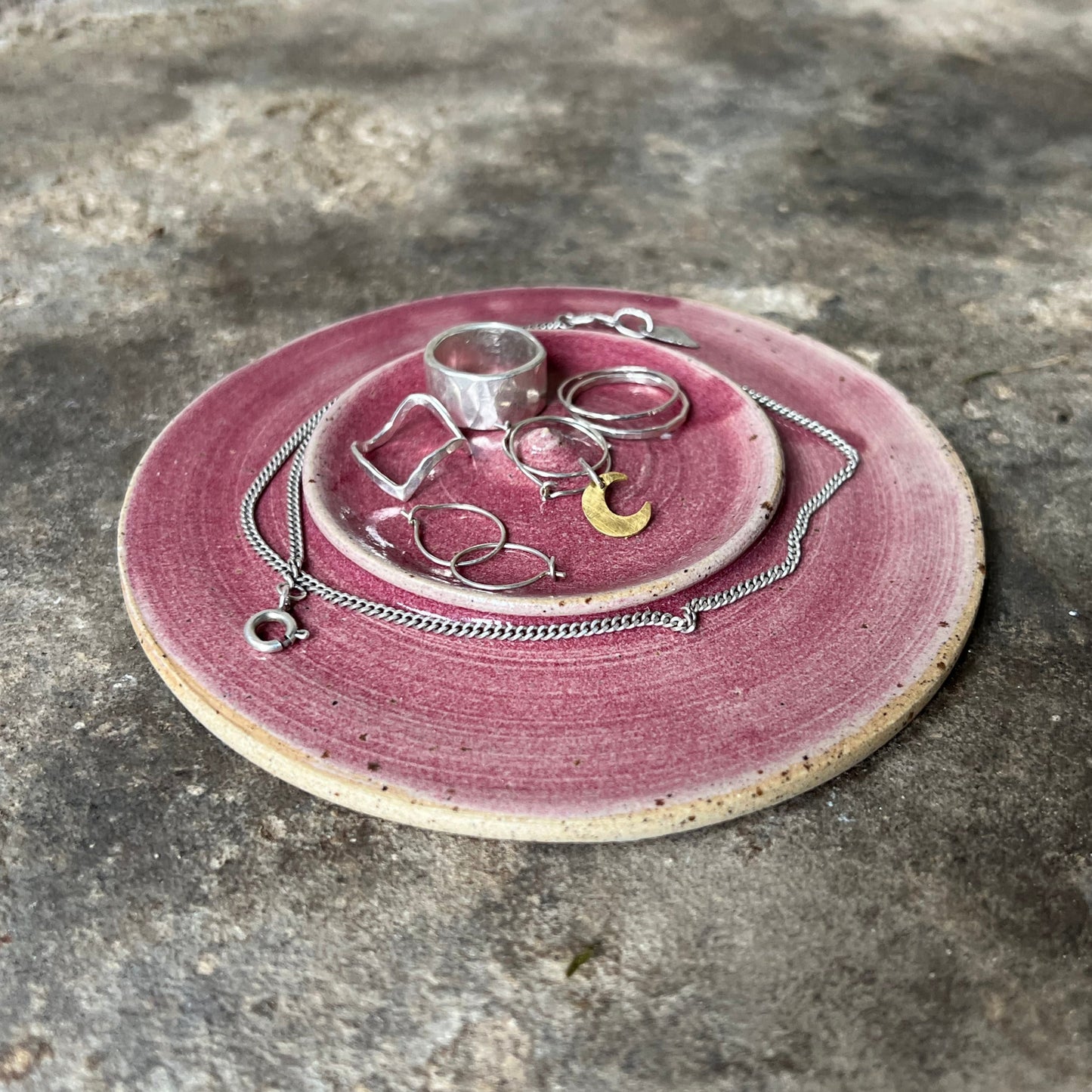 handmade Pink jewelry dish with silver rings and necklaces on a stone surface