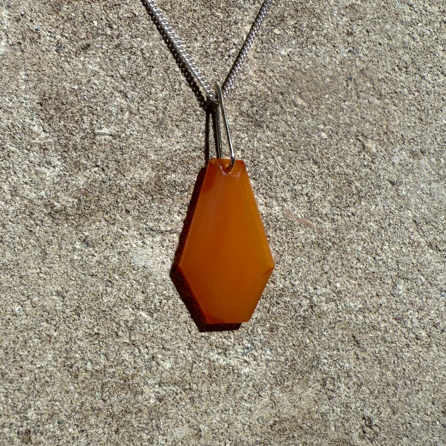 Orange hexagonal crystal pendant in a silver curb chain on a concrete surface