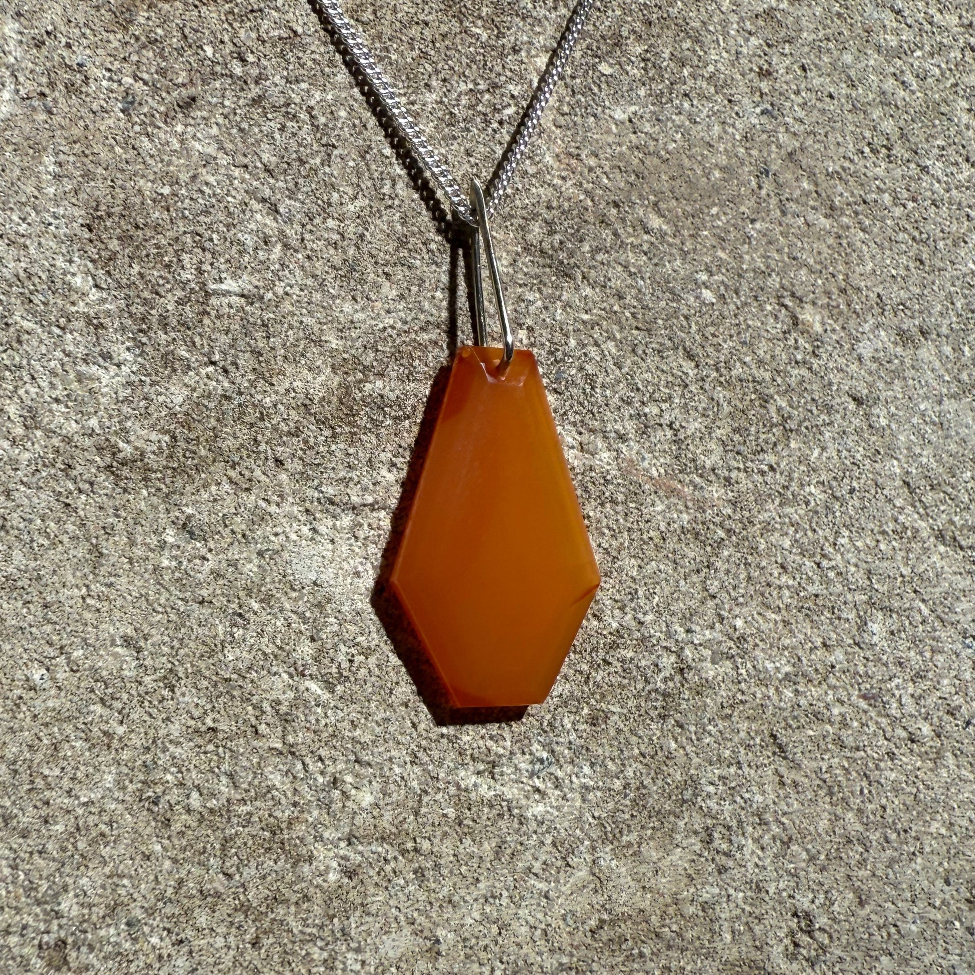 Orange hexagonal crystal pendant in a silver curb chain on a concrete surface