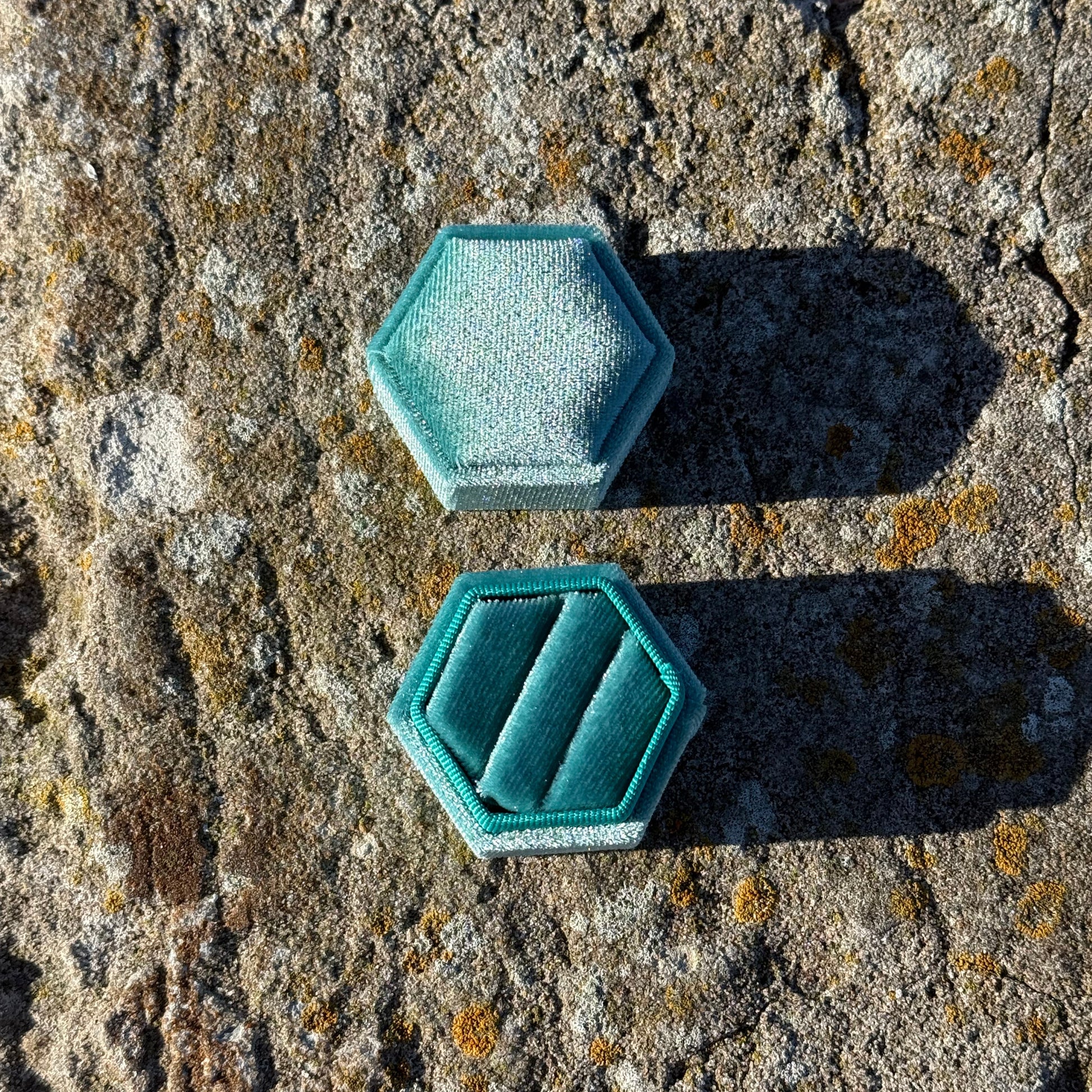 hexagonal teal velvet jewelry box on a textured stone surface