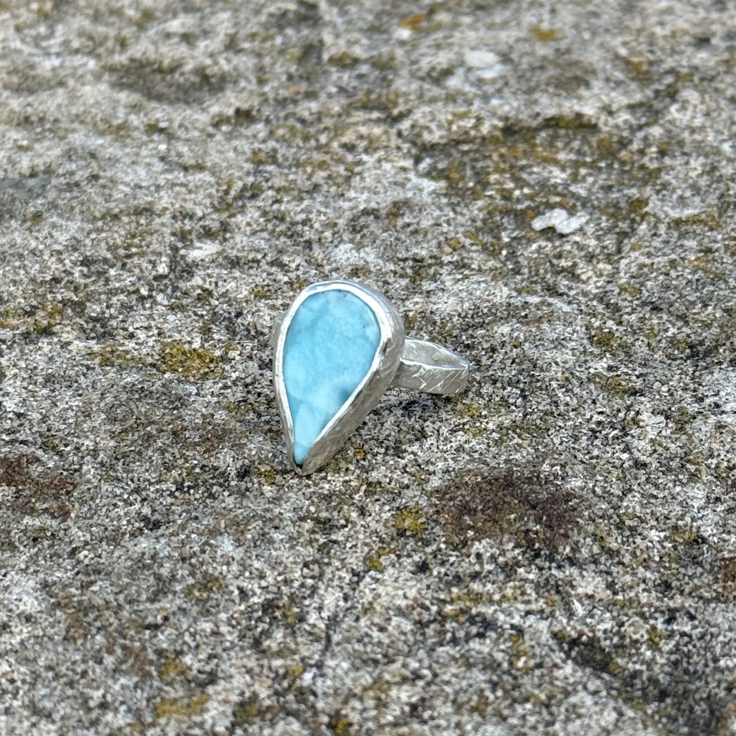 dropshaped larimar stone embedded in a band of silver 925 on a textured gray surface