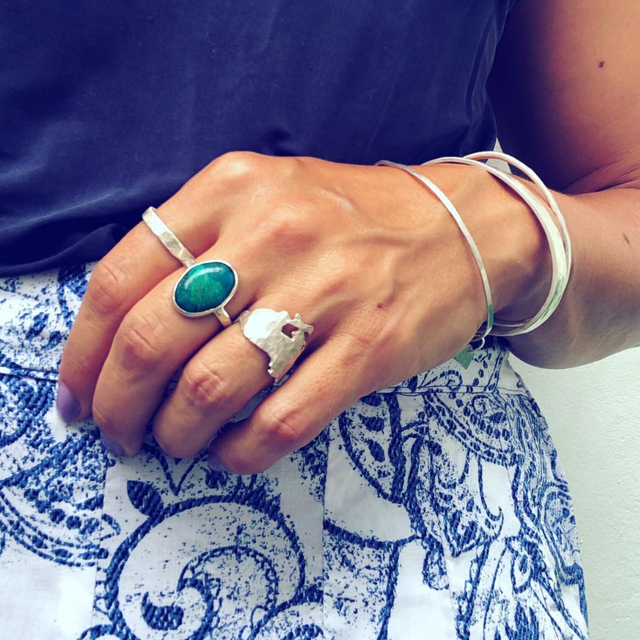 Close-up of a hand wearing silver rings with a green stone on a blue and white patterned fabric background.