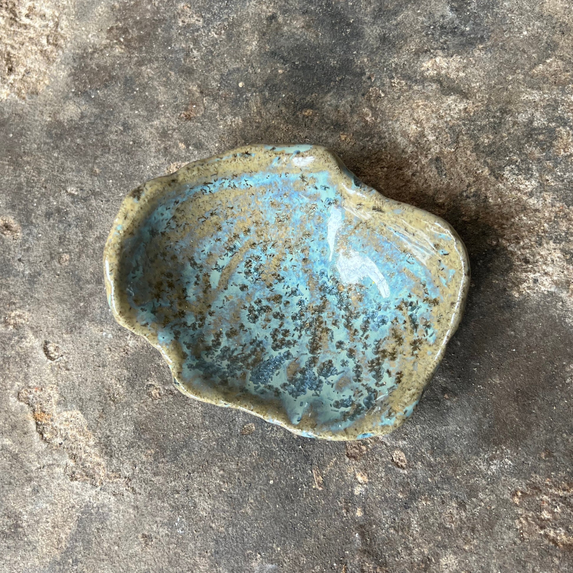Small ceramic dish with blue speckled glaze on a textured stone surface