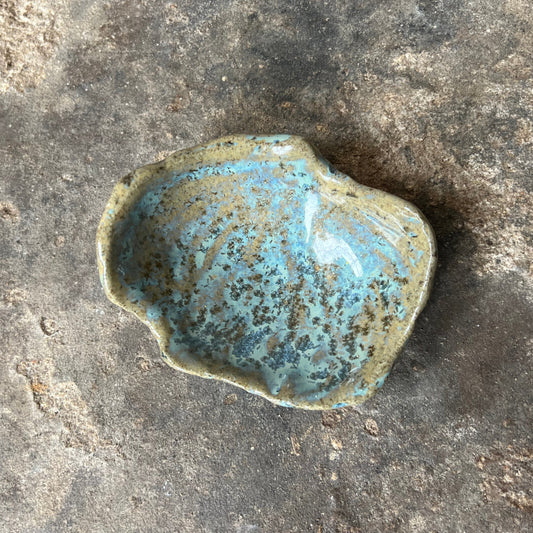 Small ceramic dish with blue speckled glaze on a textured stone surface