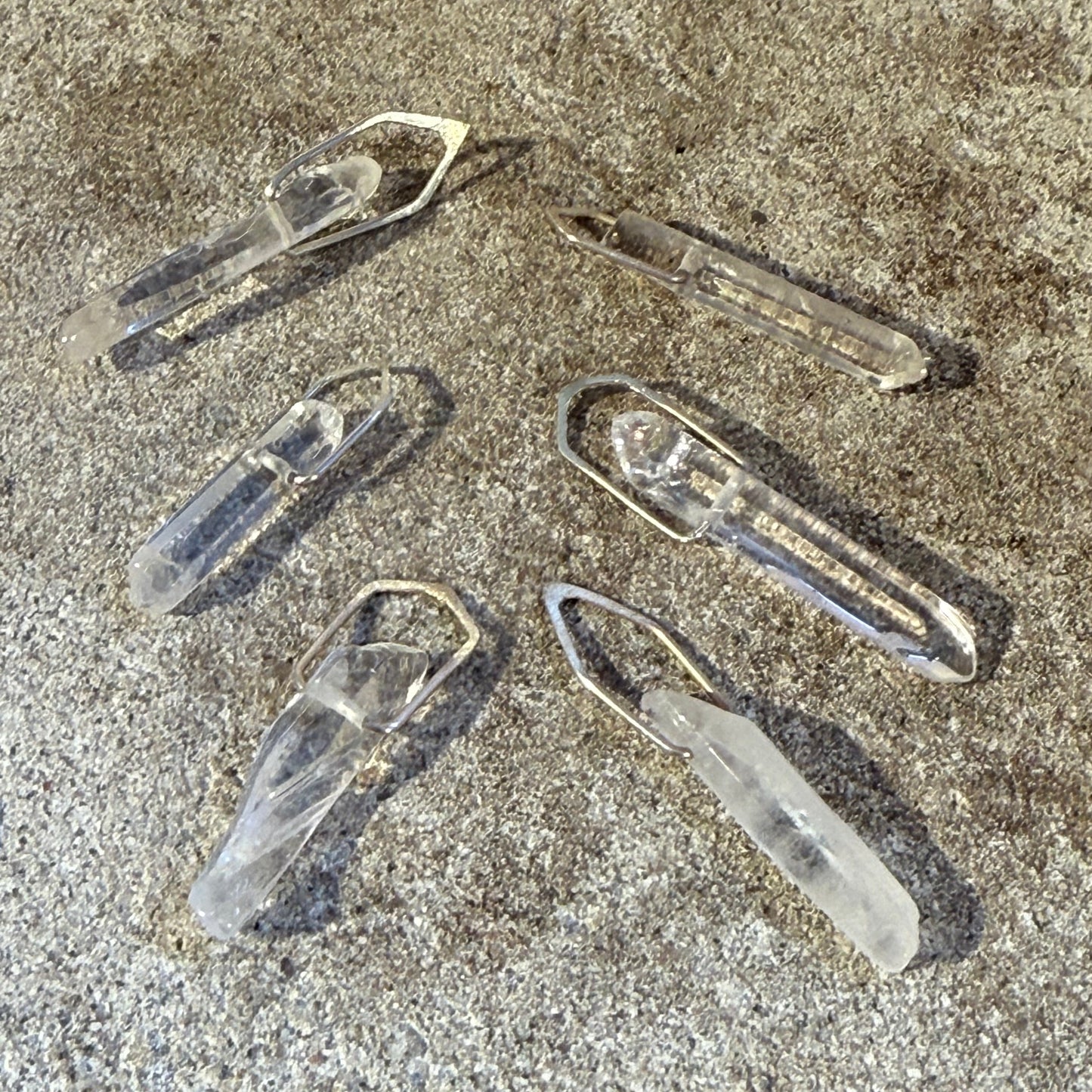 Clear Quartz silver pendants on a textured stone surface