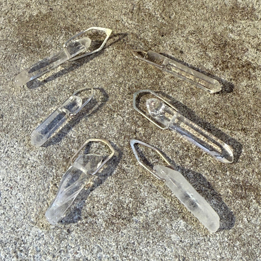 Clear Quartz silver pendants on a textured stone surface