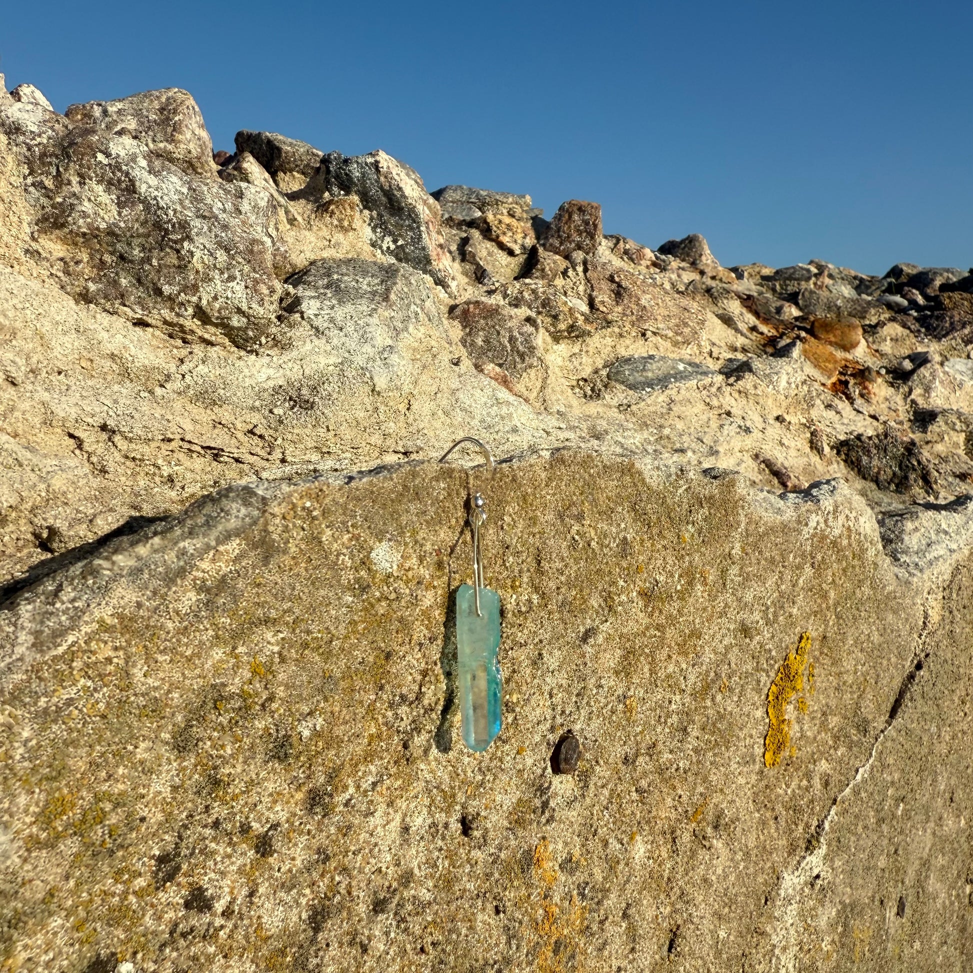 turqoise mono earring on a rocky surface with clear blue sky