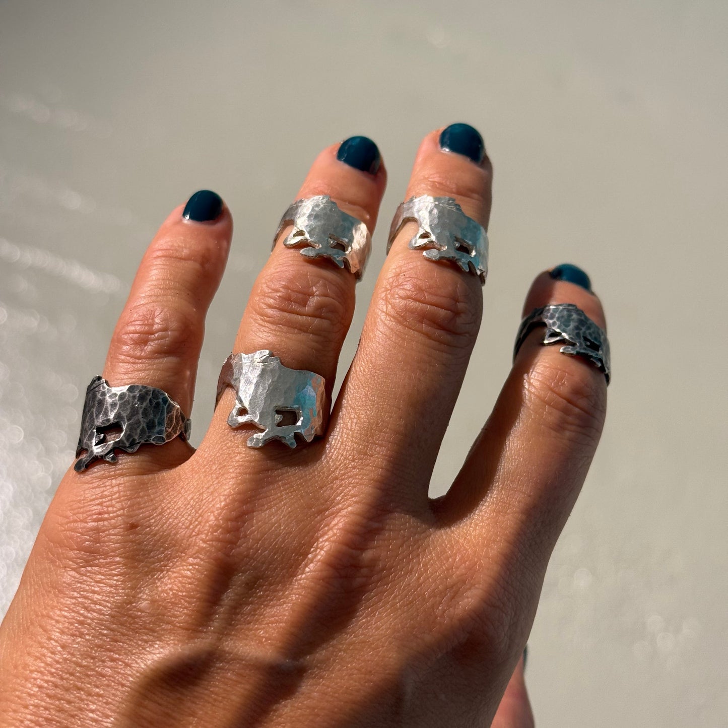 Hand wearing multiple mustang silver rings on a neutral background