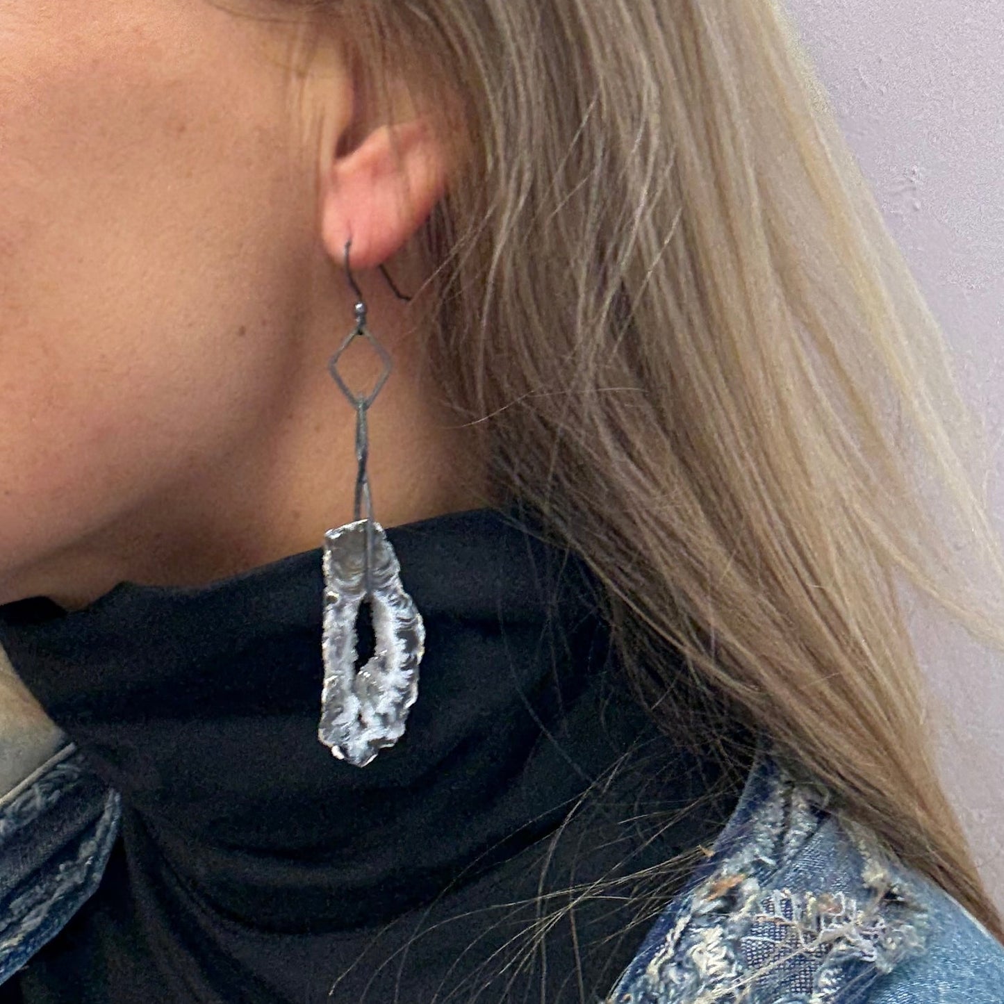 Person wearing a denim vest with a druzy agate earring in oxidized silver