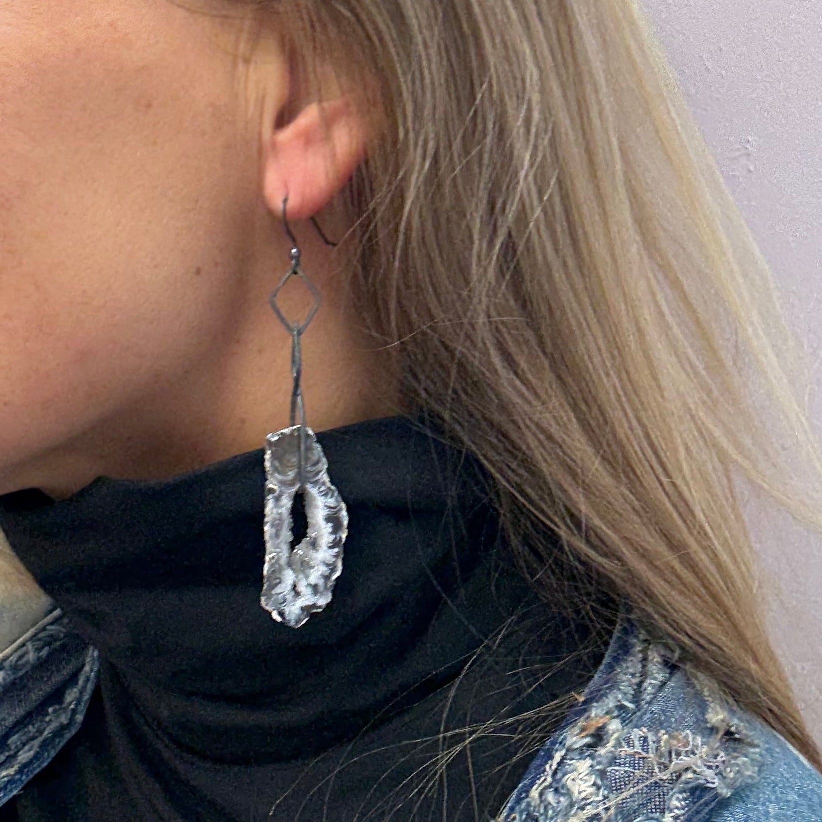 Person wearing a denim vest with a druzy agate earring in oxidized silver