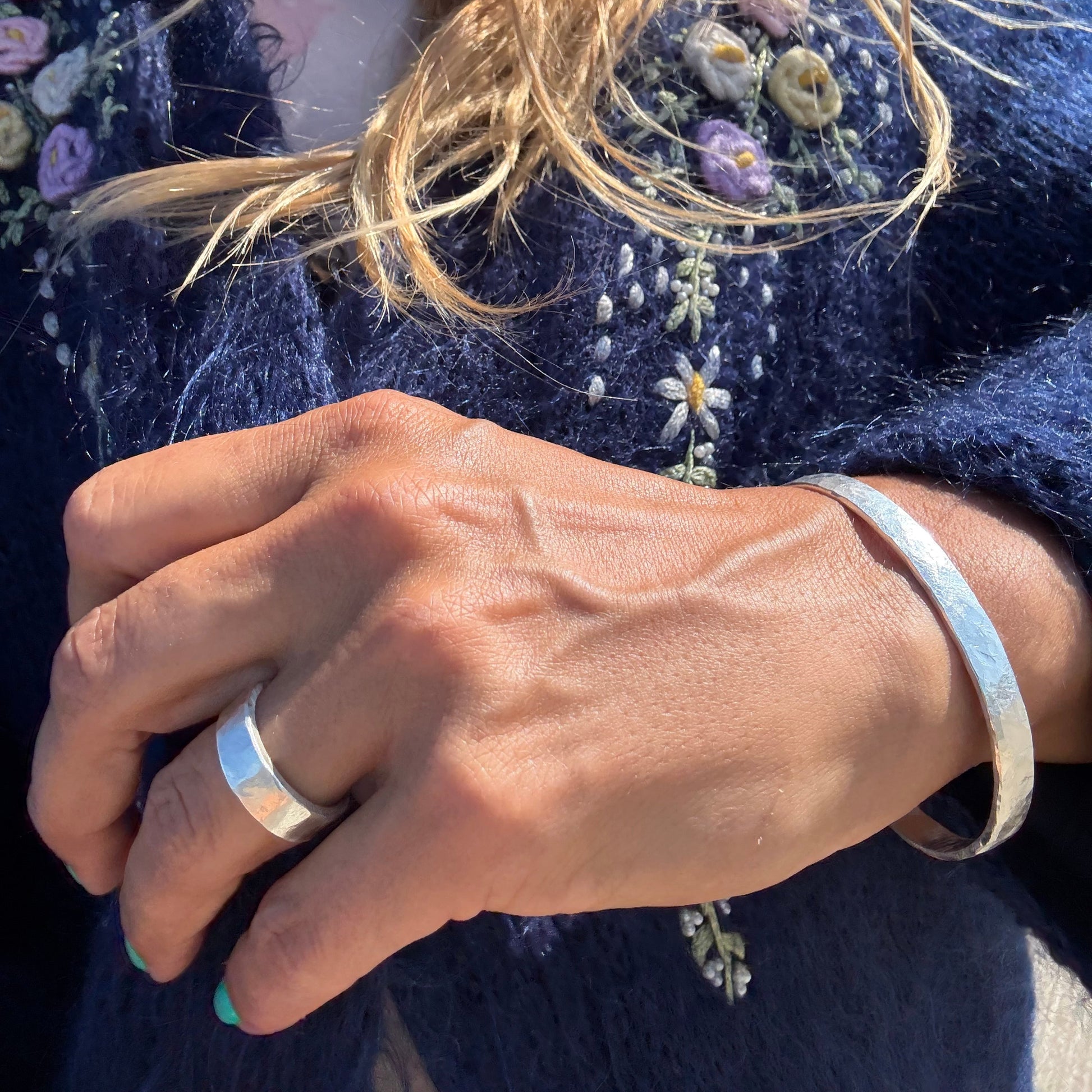 Close-up of a hand wearing a silver ring and a silver cuff with a blue embroidered garment in the background