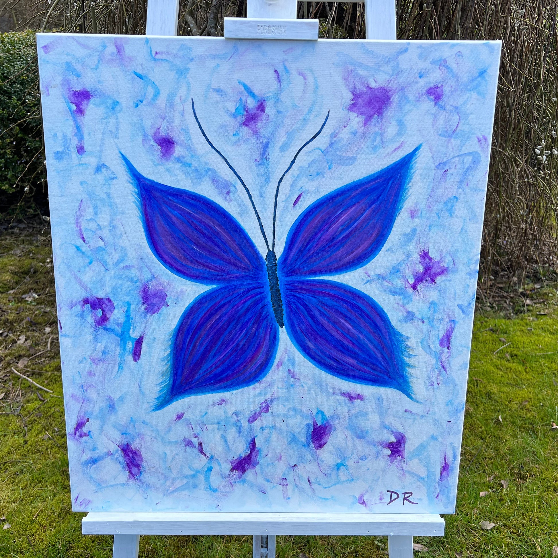 Painting of a blue butterfly on a light blue background with purple accents, displayed outdoors.