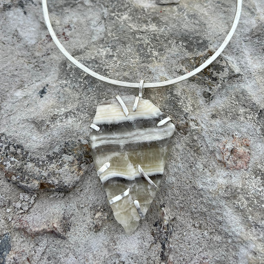 Silver neck ring and zebra calcite pendant on a textured stone surface