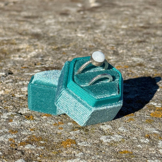 Teal hexagonal jewlry box in velvet holding two rings