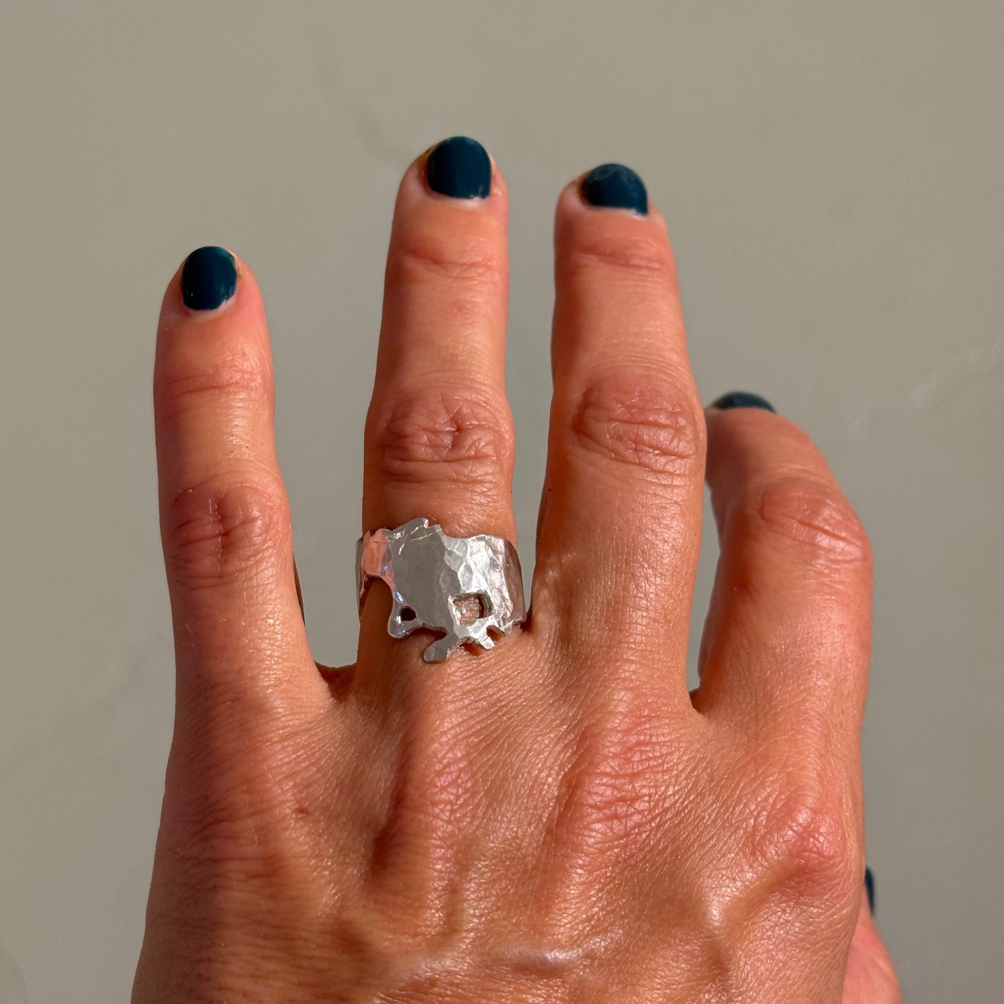Hand wearing a silver mustang ring on a neutral background