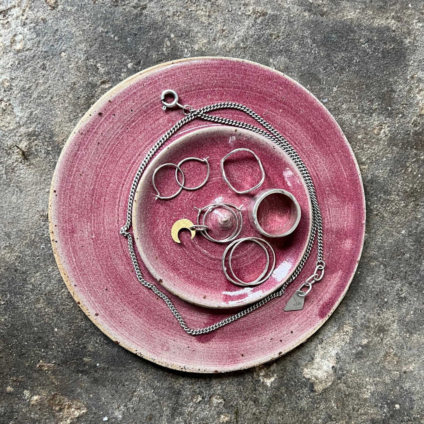 Pink ceramic plate with jewelry on a textured gray surface