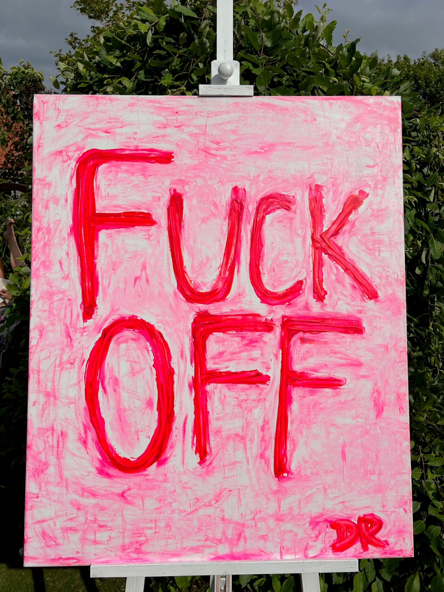 Neon Pink sign with text 'FUCK OFF' on a white stand outdoors.