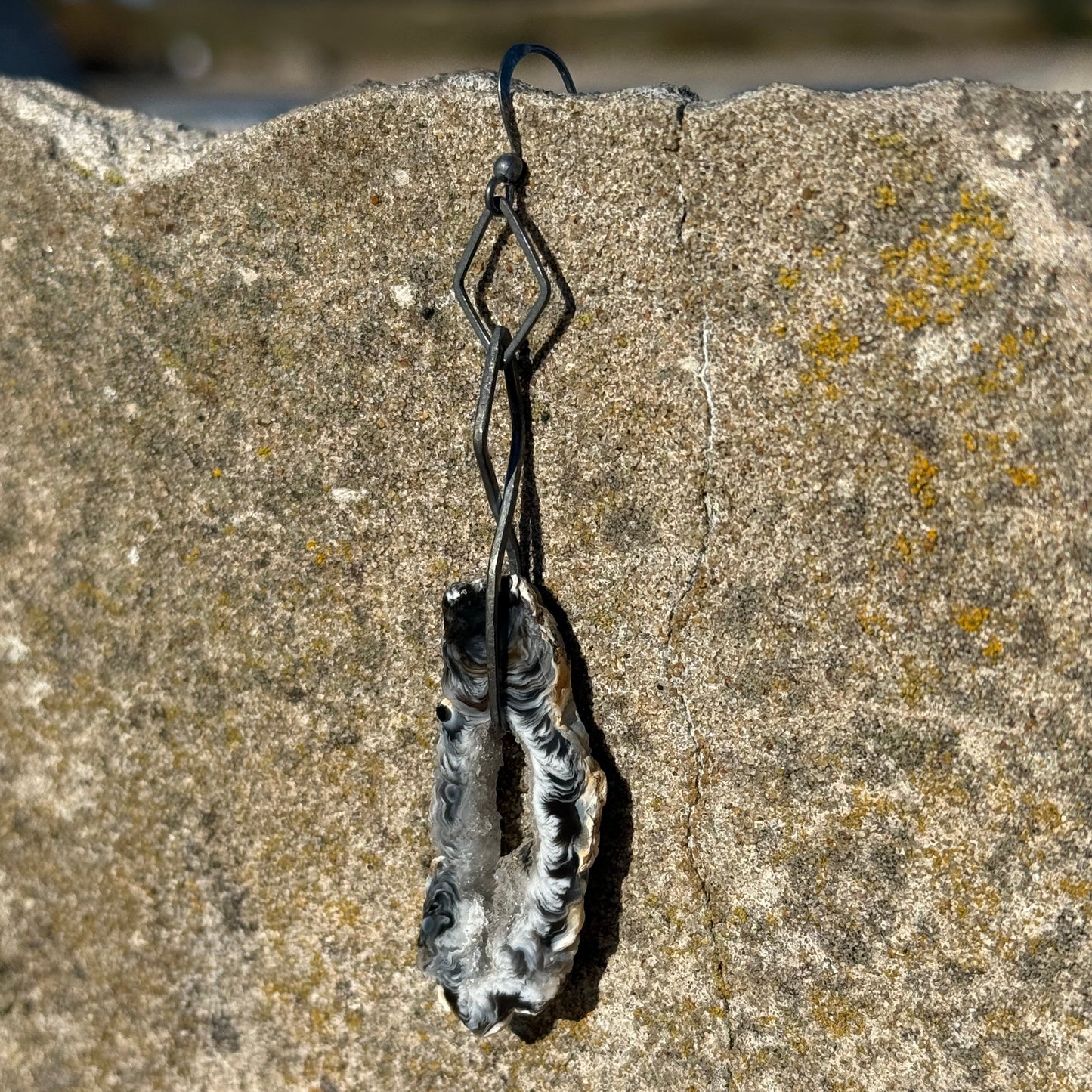 dangling oxidized silver earring with druzy agate on a textured stone surface