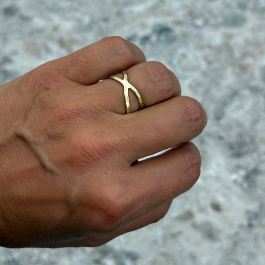brass cross ring on a person's finger against a blurred concrete background