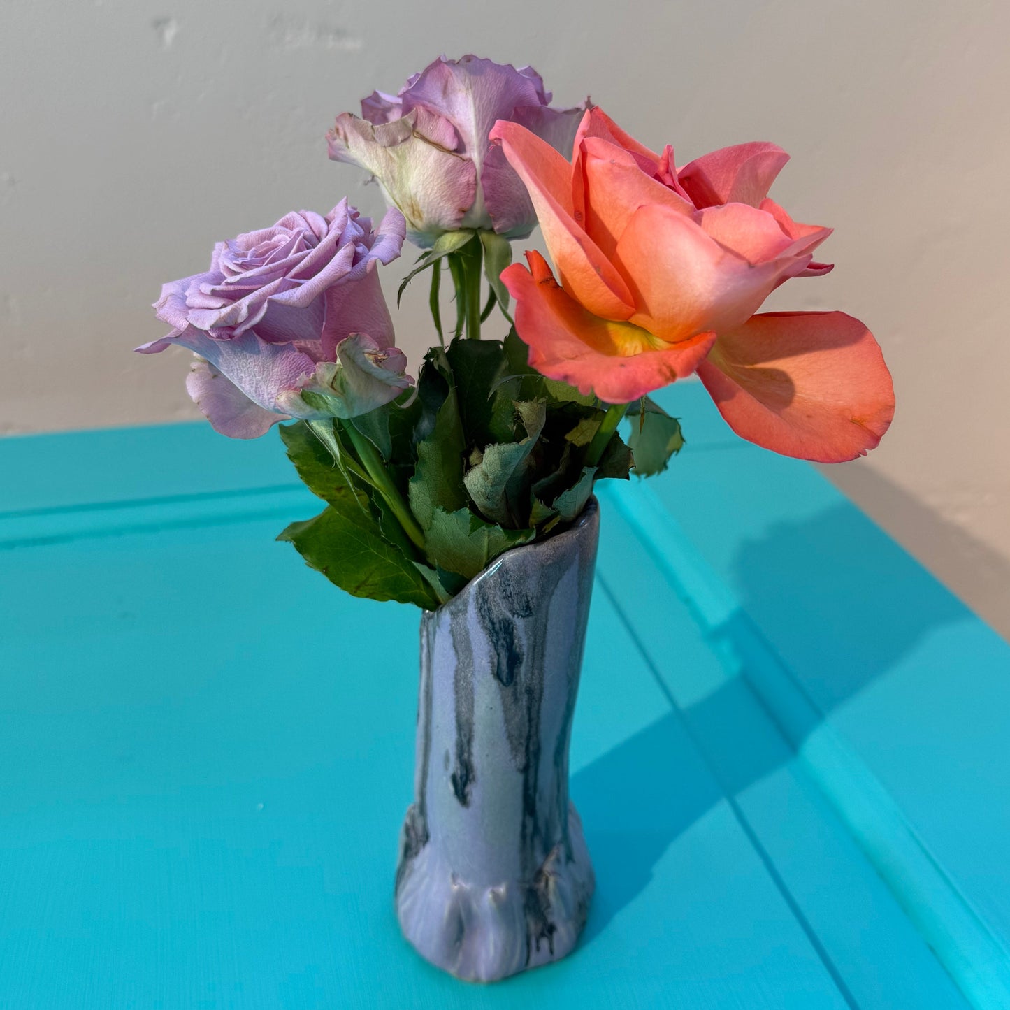 Bouquet of colorful roses in a purple and black ceramics vase on a turquoise door