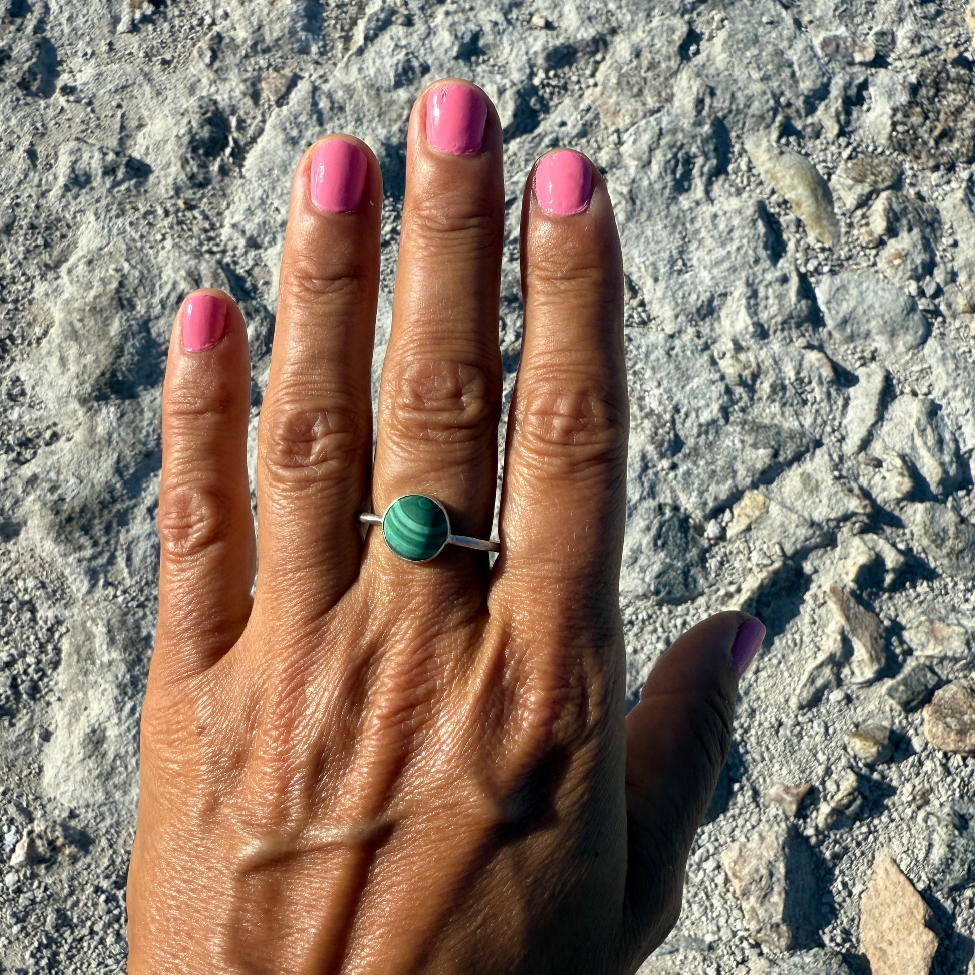 Hand with pink nail polish wearing a green ring on a textured surface