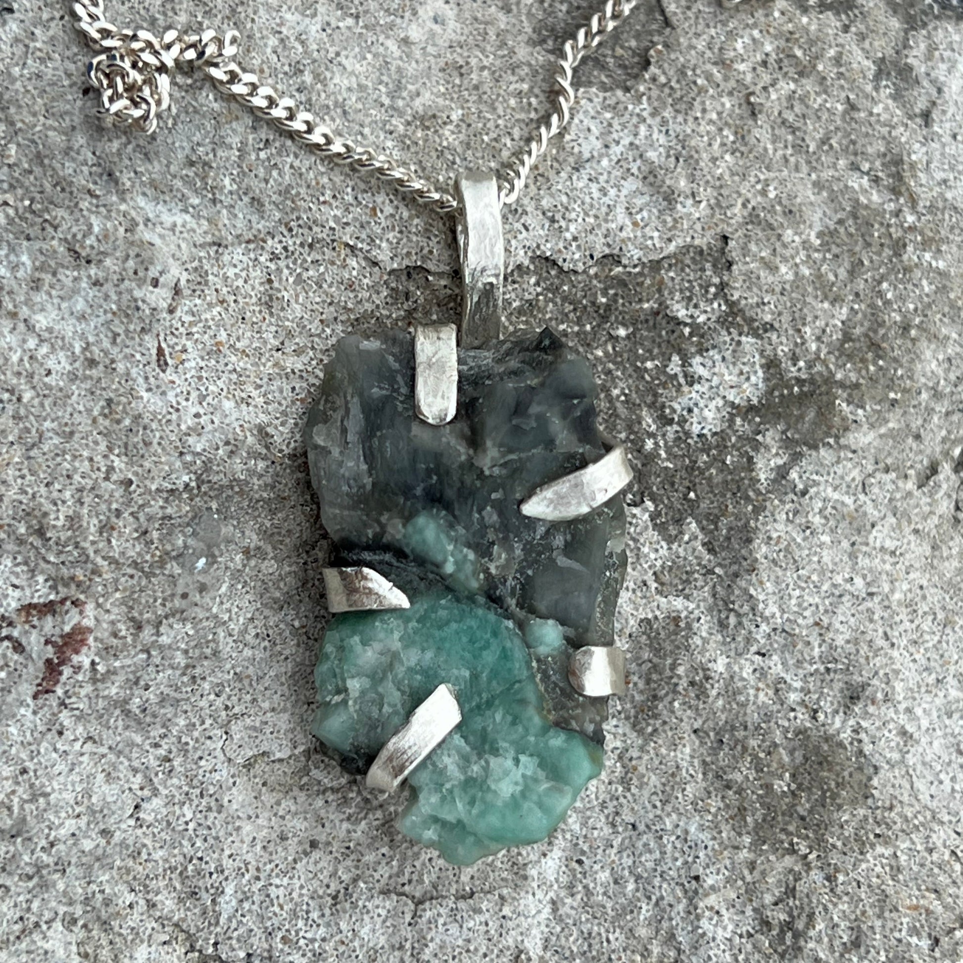 Necklace with a raw emerald in sterlingsilver pendant on a textured surface