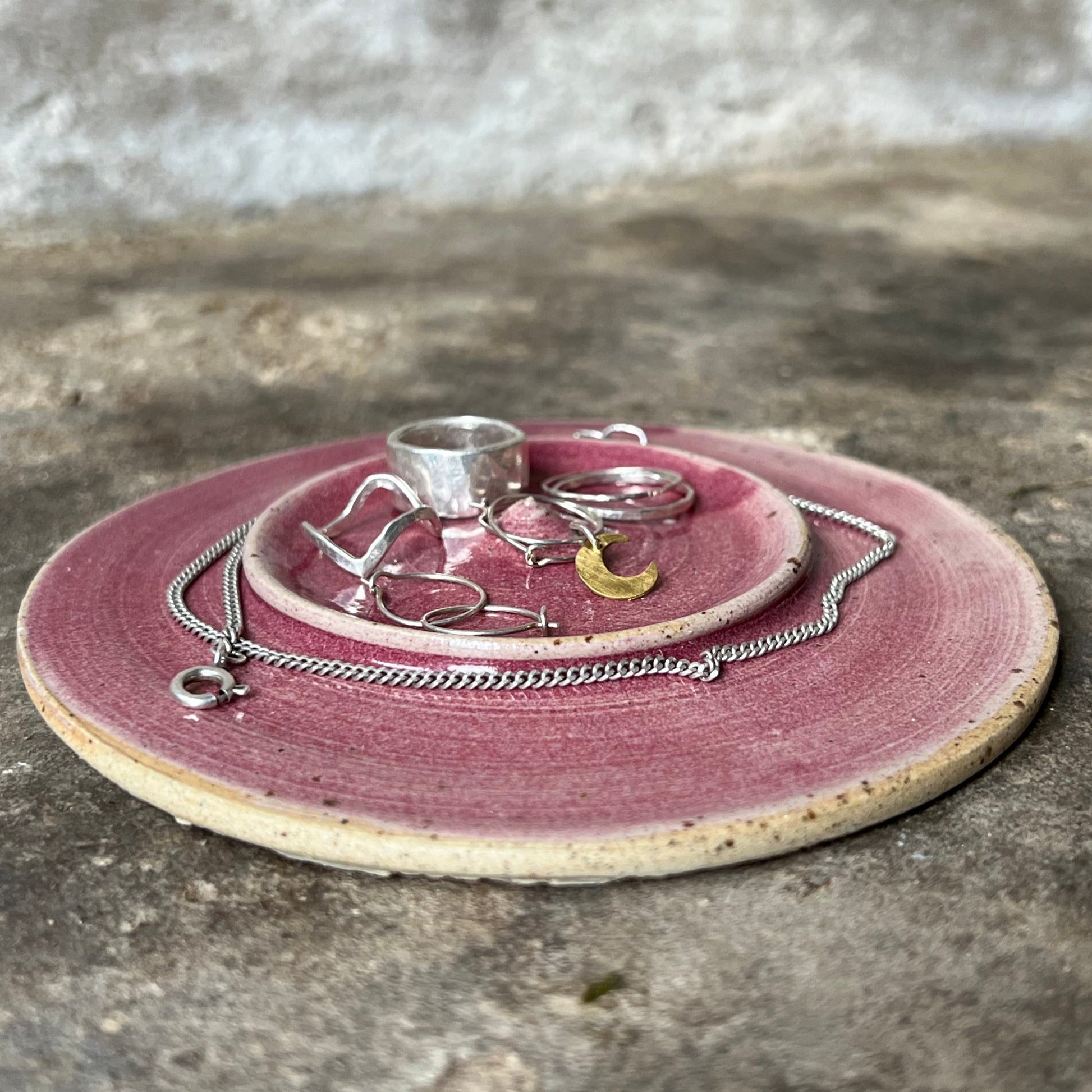 Round pink jewelry tray with jewelry on a concrete surface