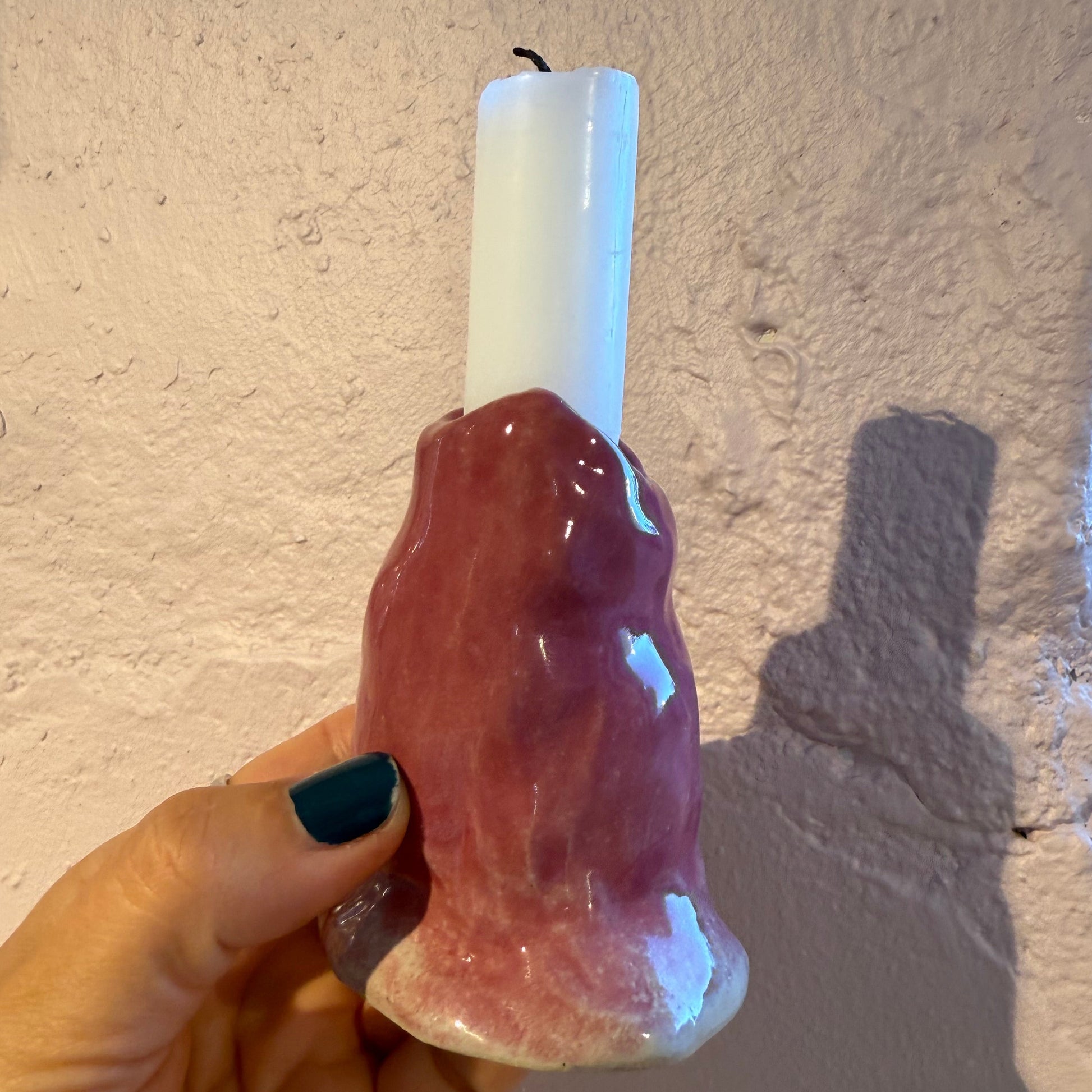 Hand holding a pink ceramic candle holder with white candle against a textured soft pink background