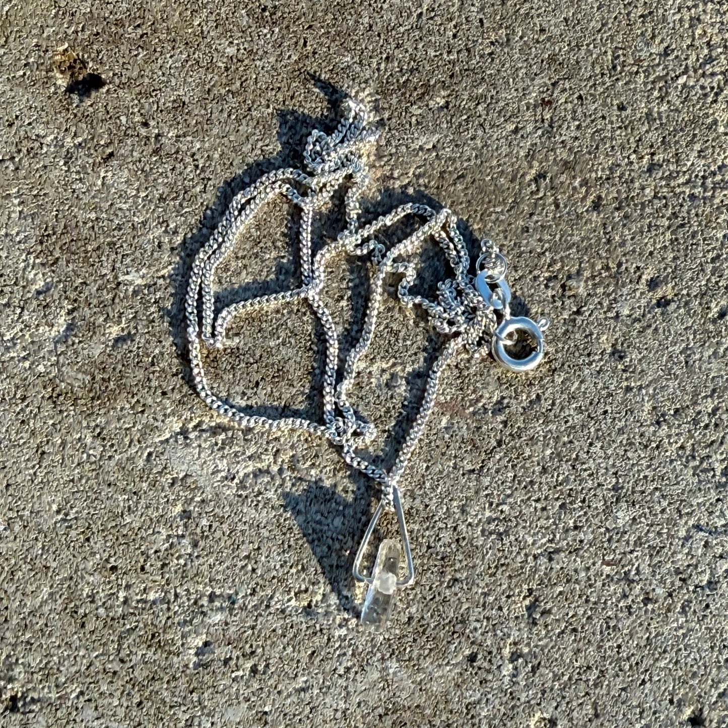 Silver necklace with a pendant lying on a textured surface