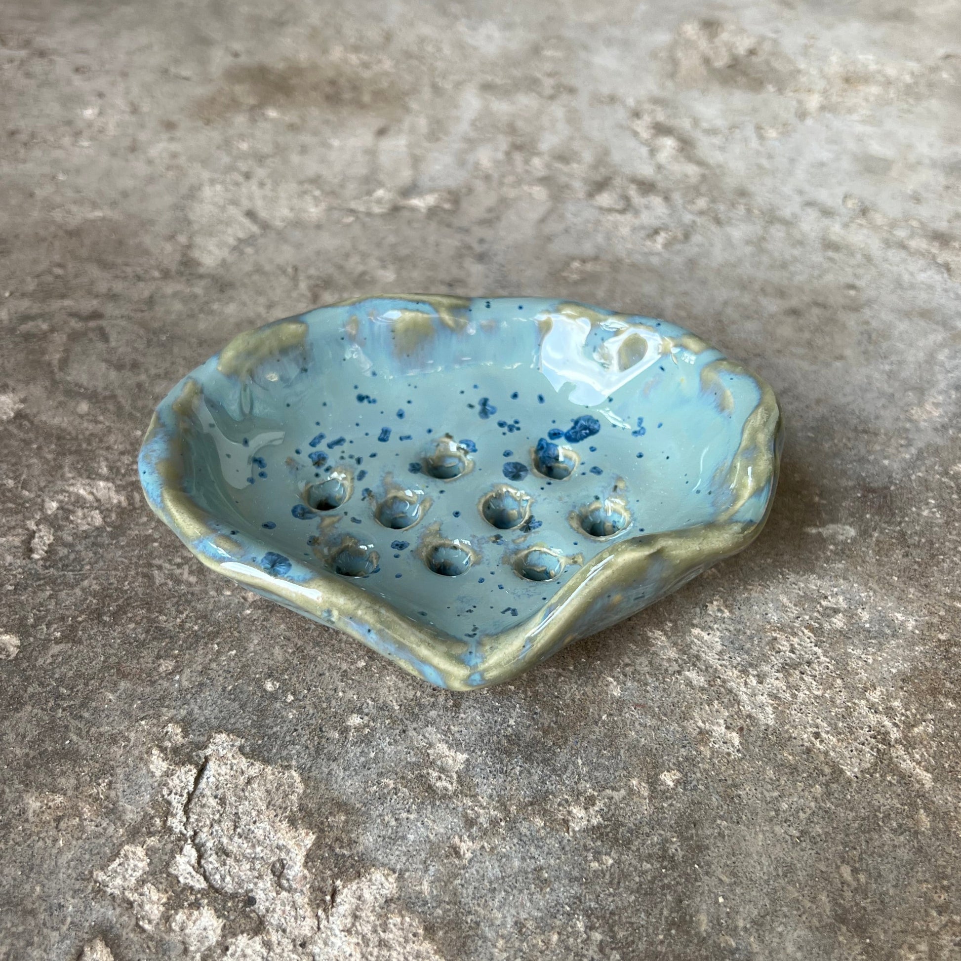 Small ceramic piece with blue glaze on a textured stone surface. Soap dish in blue spotted ceramic glaze for hard soap.