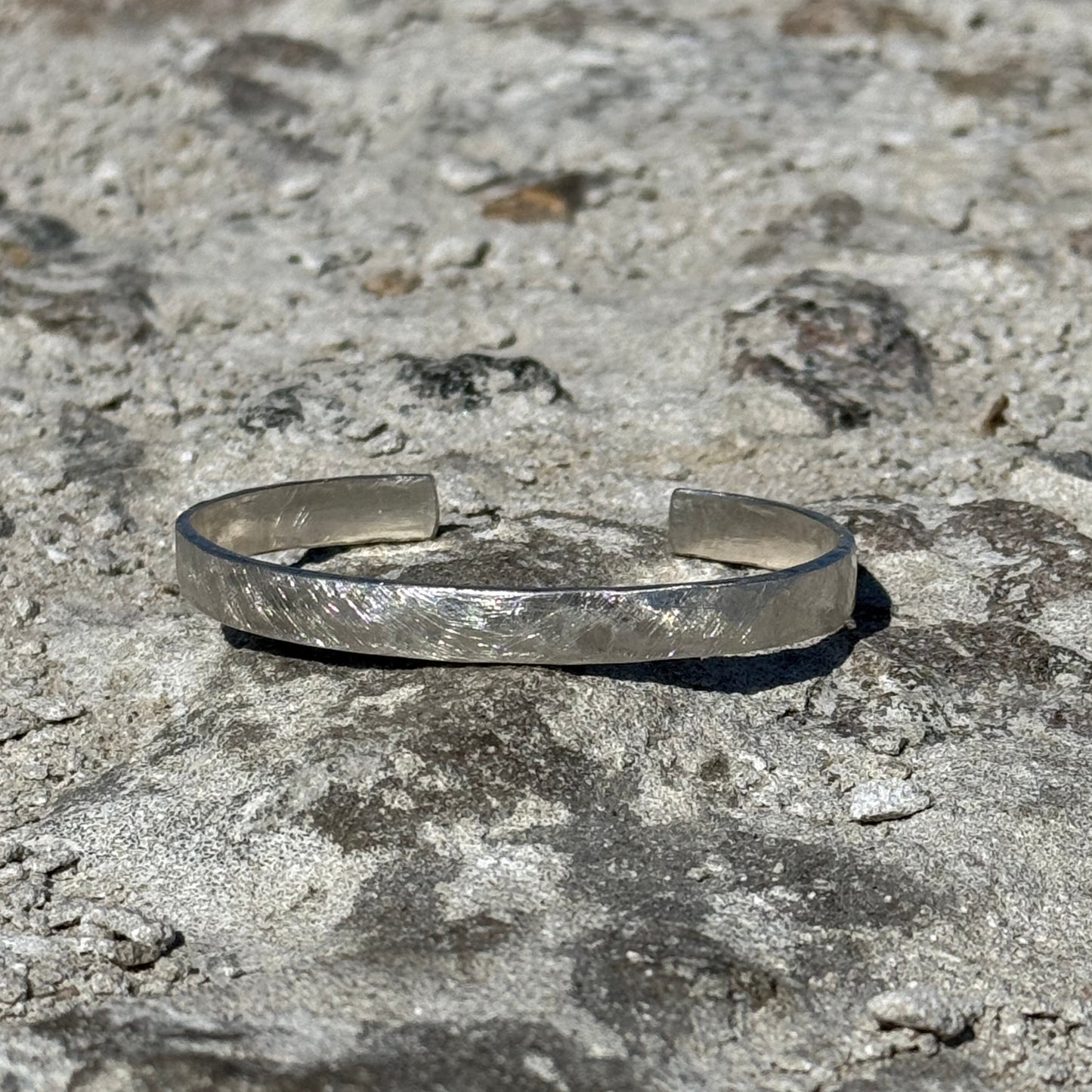 hammered unisex Silver cuff bracelet on a textured stone surface