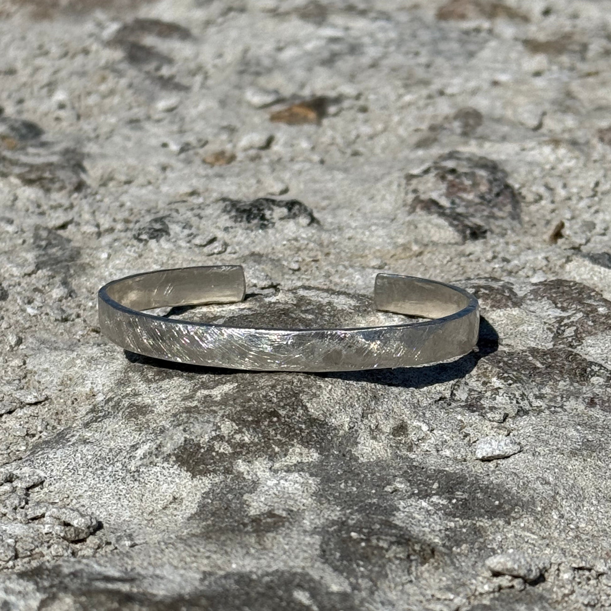 hammered unisex Silver cuff bracelet on a textured stone surface