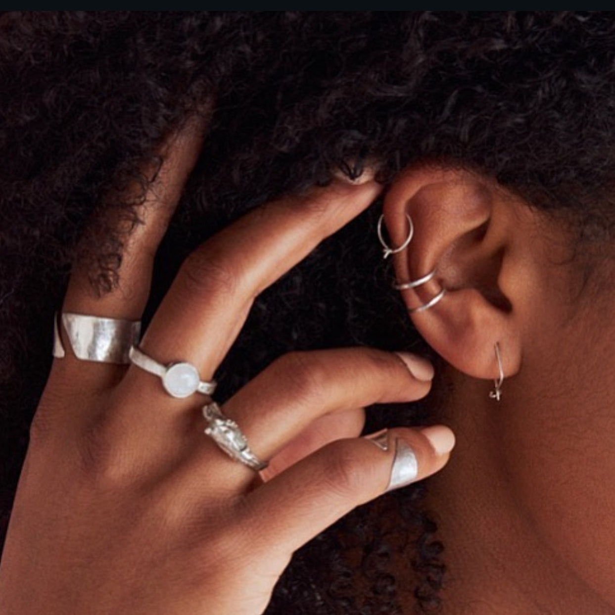 Close-up of a hand with multiple rings touching an ear wearing earrings.