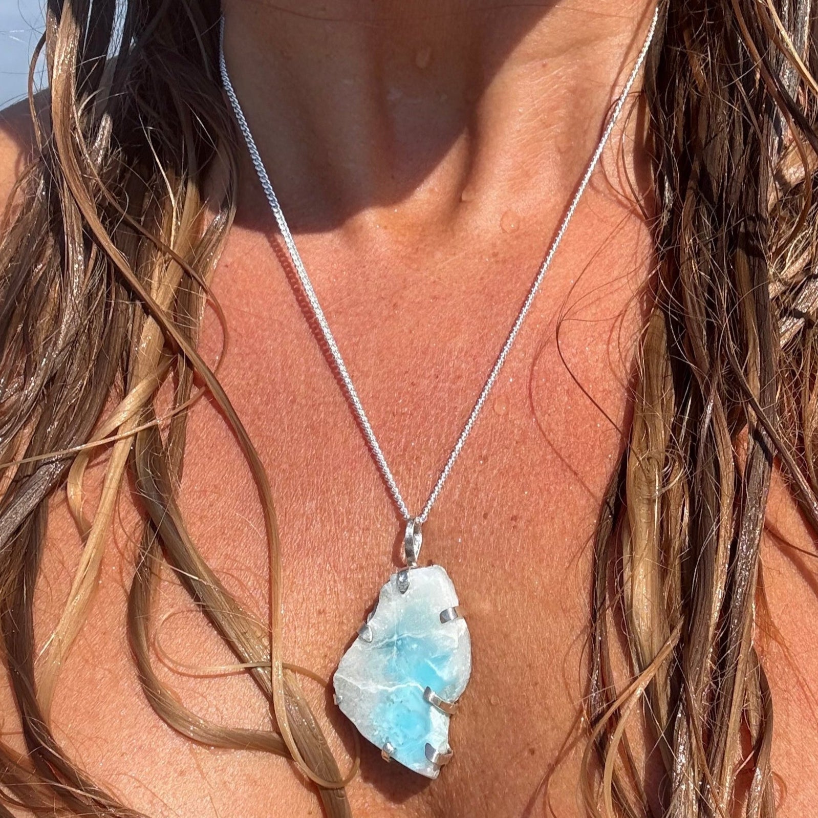 Close-up of a silver necklace with a blue pendant worn by a person with long hair.