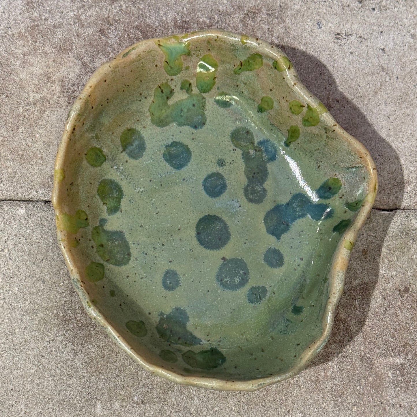 Green ceramic seashell bowl with speckled pattern on a concrete surface