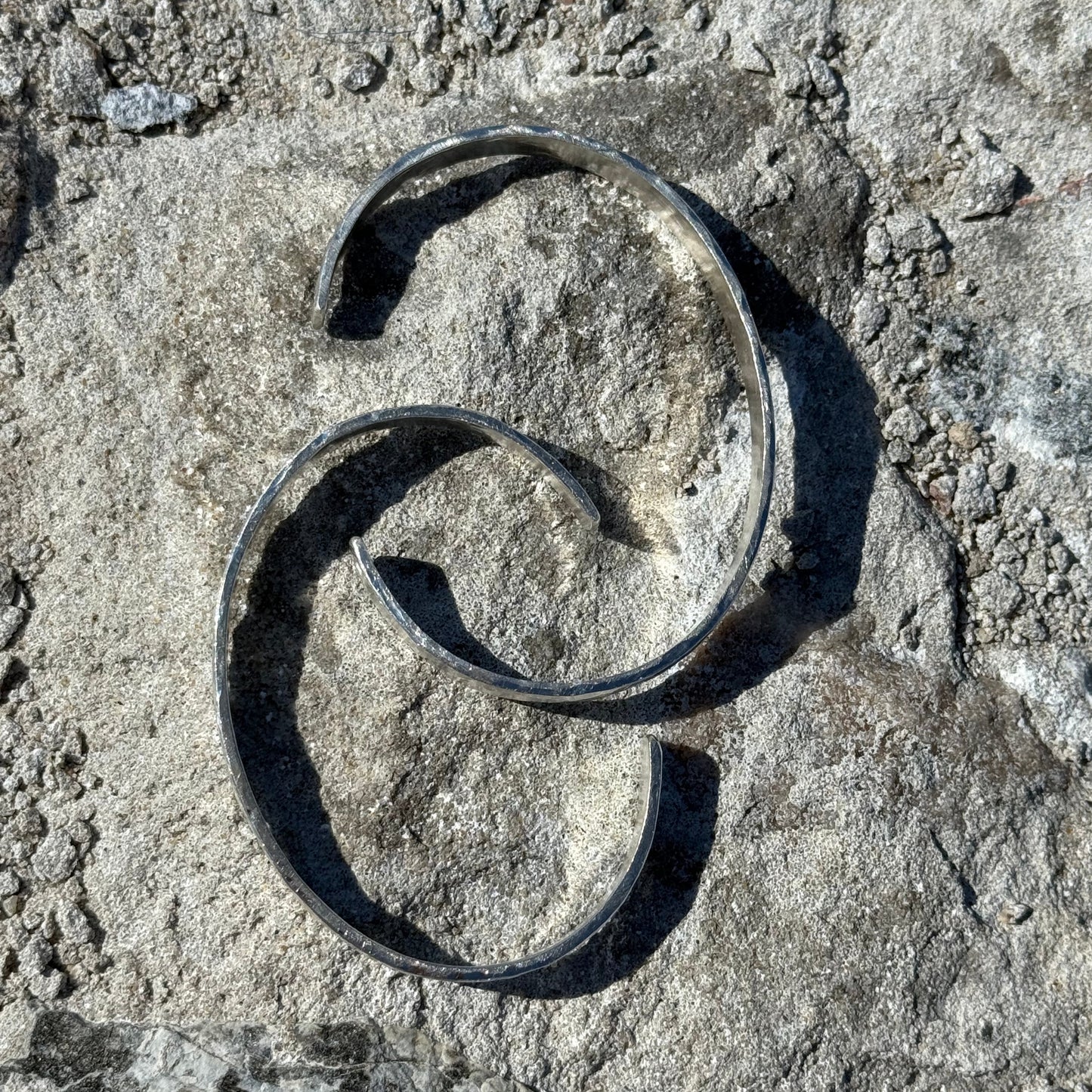 Two silver cuffs on a textured stone surface