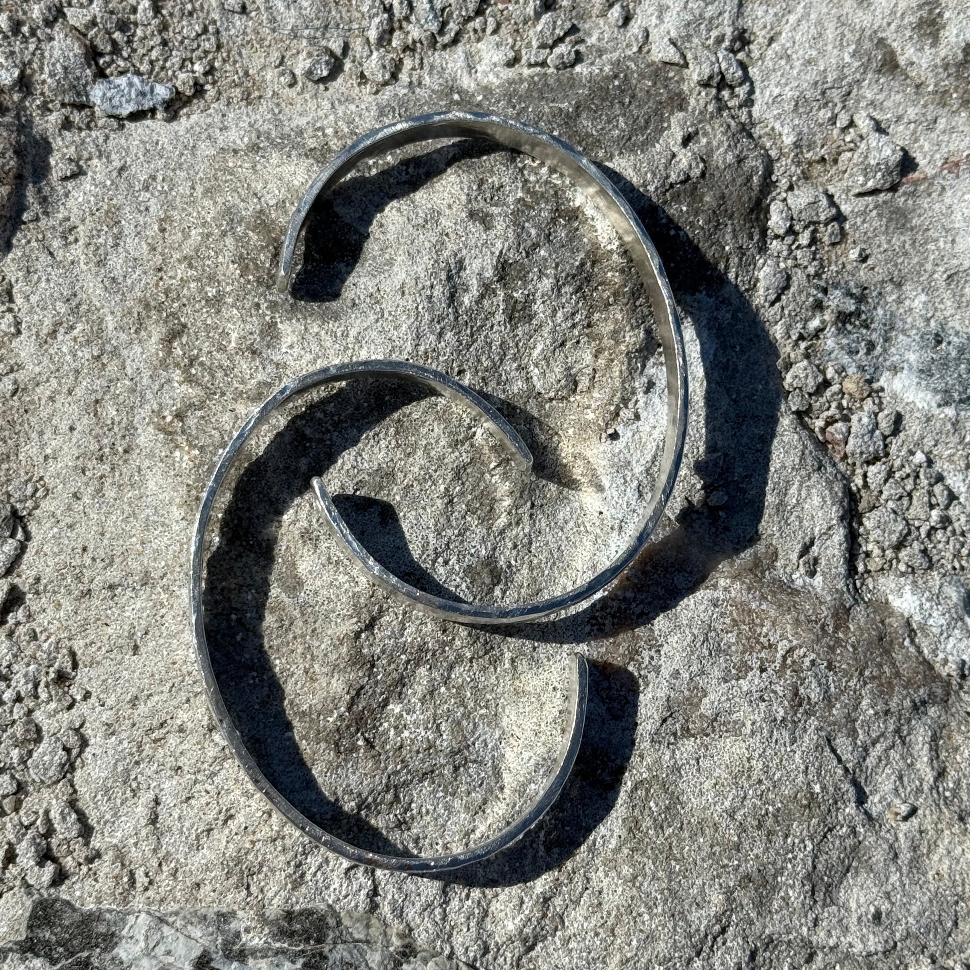 Two silver cuffs on a textured stone surface