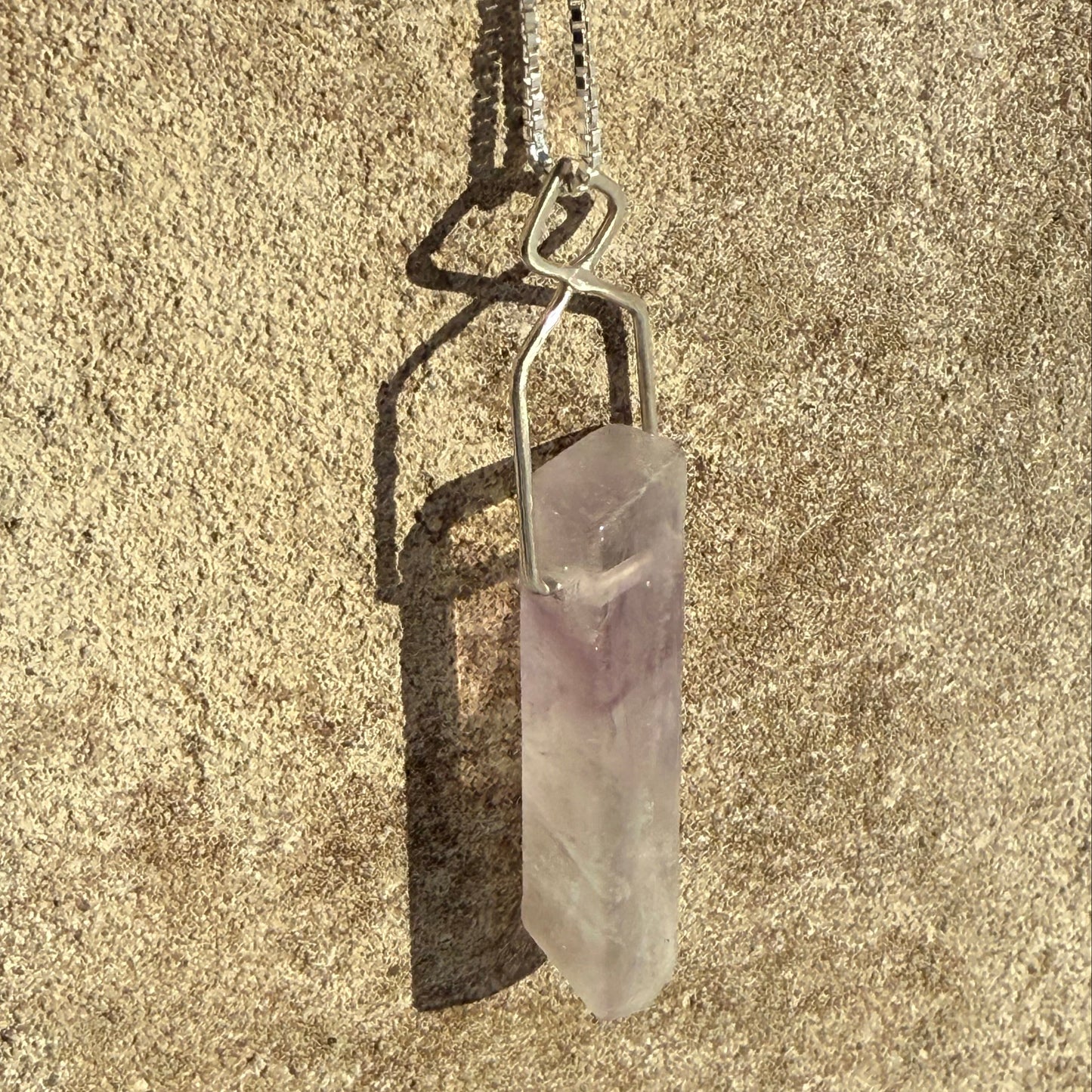Crystal pendant on a chain lying on sandy ground