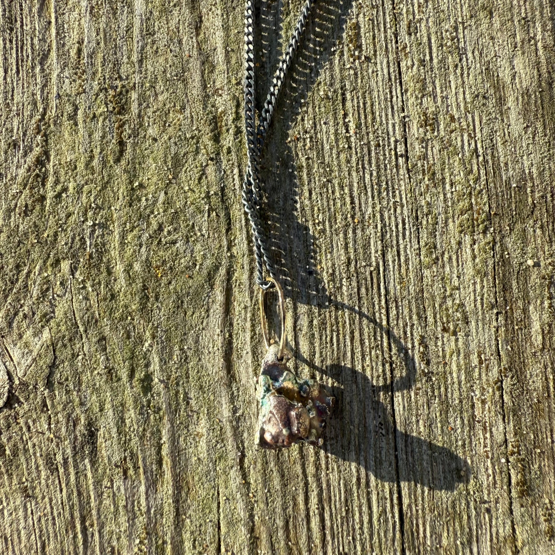 blackened silver curb chain necklace with organically crafted silver pendant on wooden surface