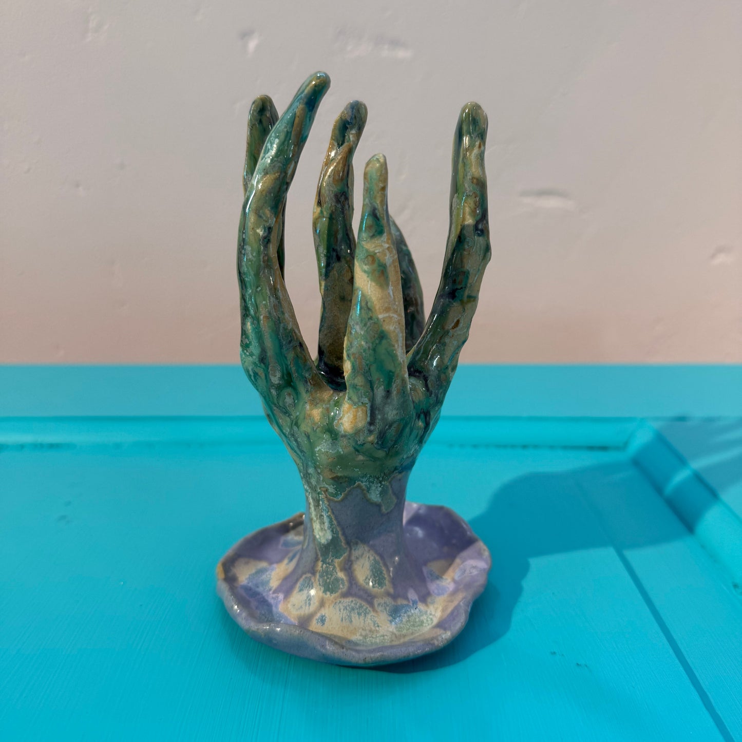 Decorative hand-shaped jewelry holder object on a turquoise surface