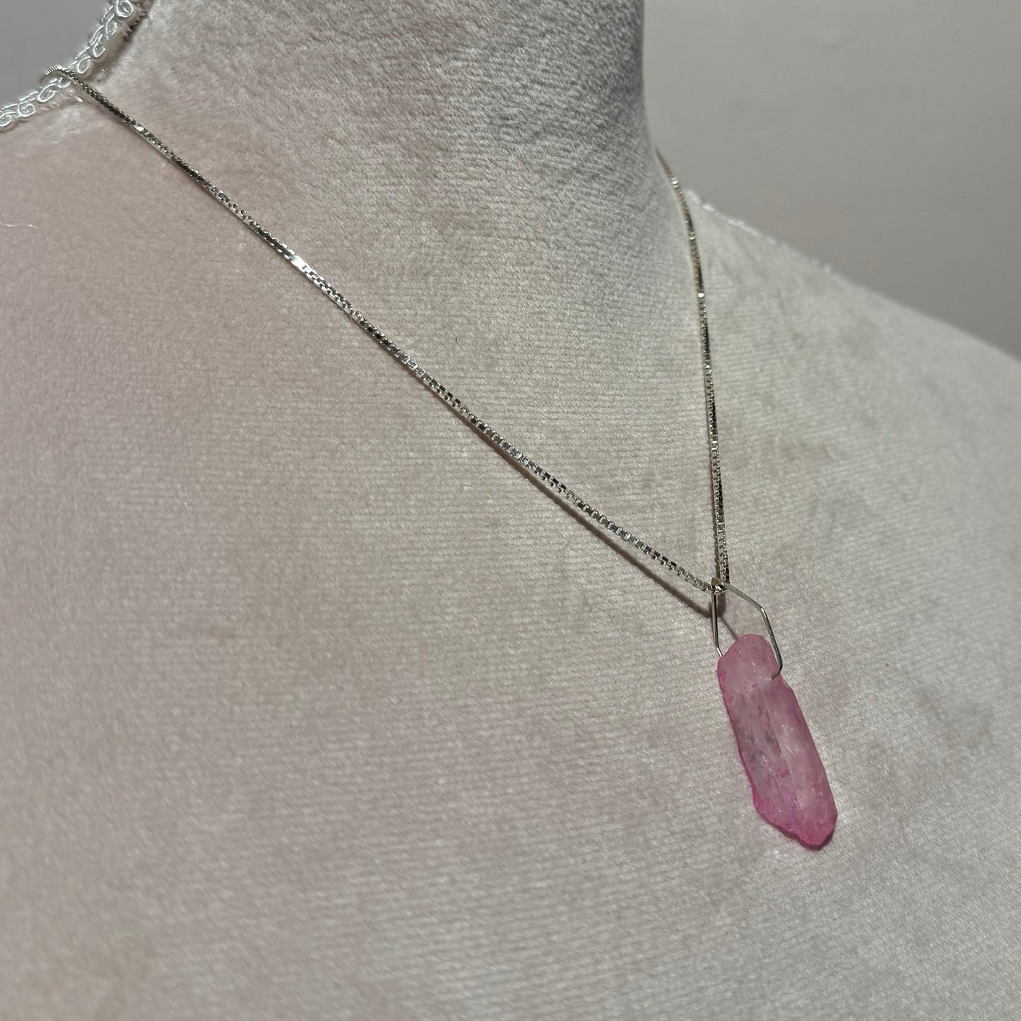 Close-up of a mannequin with a pink crystal necklace in silver on its chest against a gray background