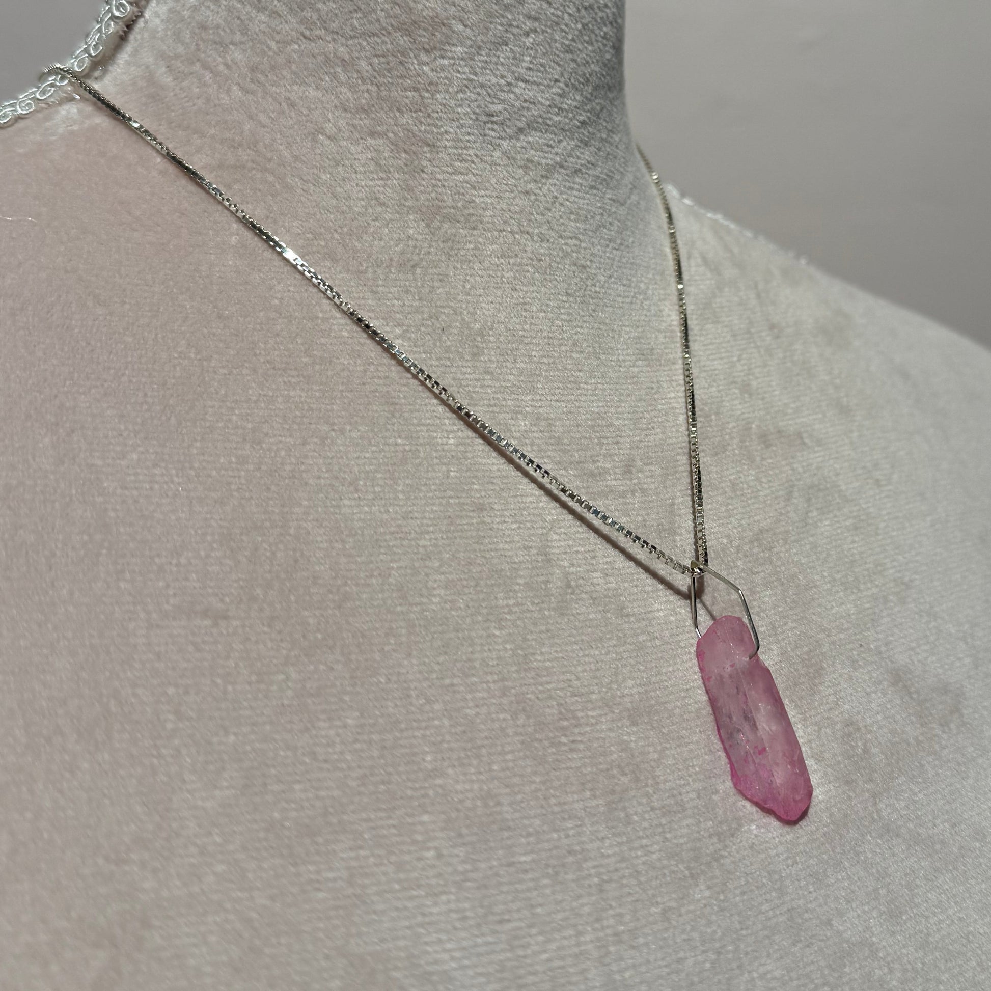 Close-up of a mannequin with a pink crystal necklace in silver on its chest against a gray background