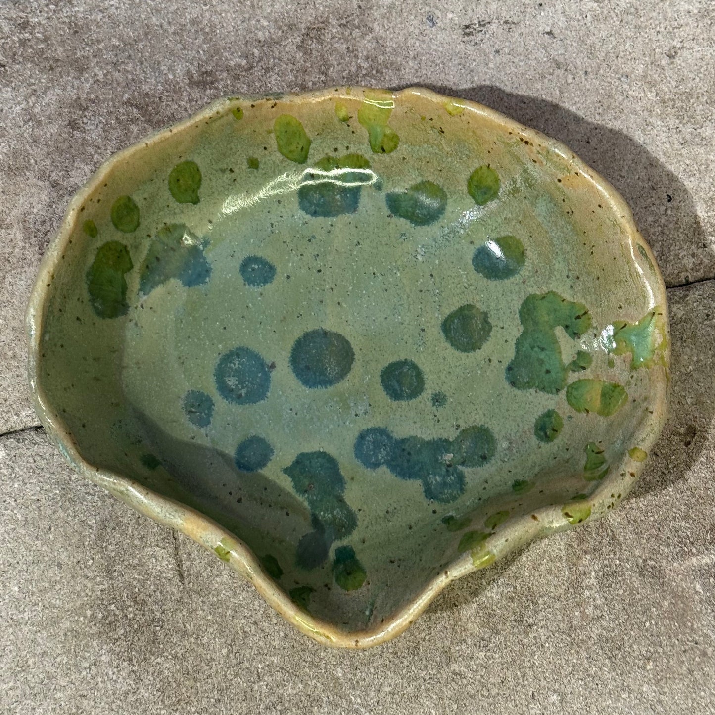 Green ceramic bowl with speckled pattern on a concrete surface
