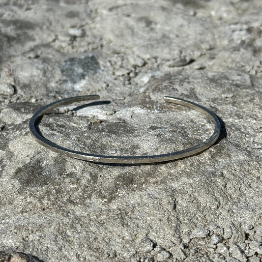 thin hammered and brushed Silver cuff on a textured stone surface